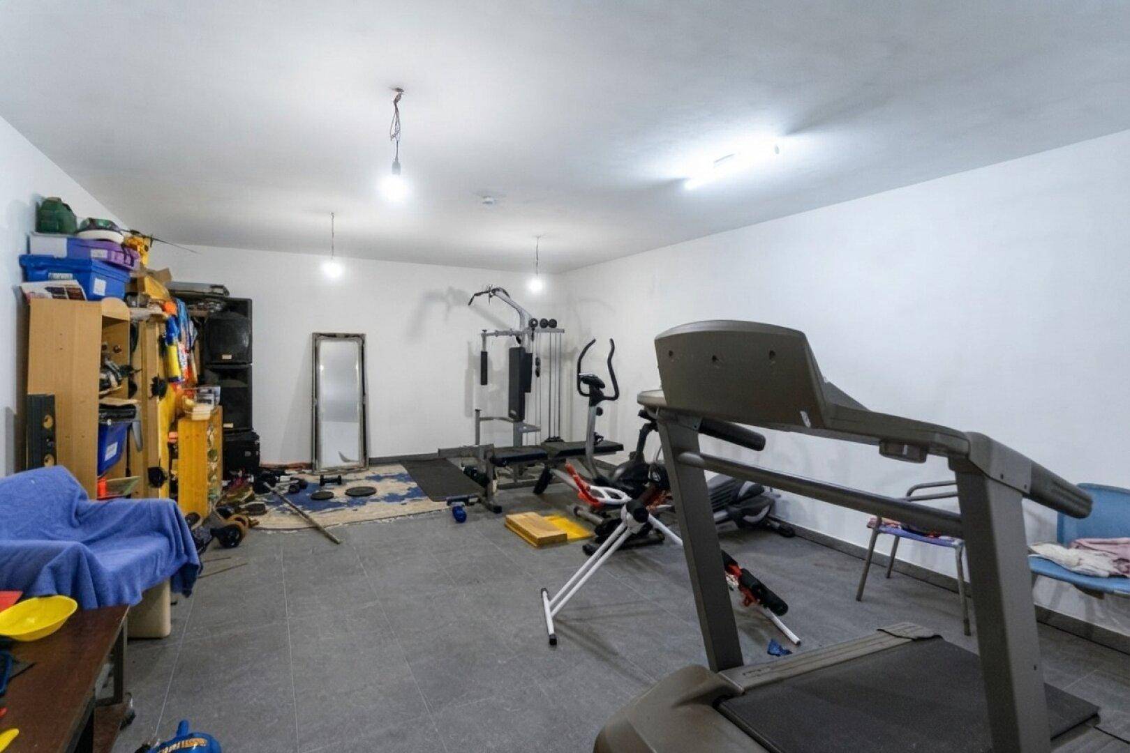 Großer Raum im Untergeschoss mit Fitnessgeräten und Stauraum, ideal für Sport.