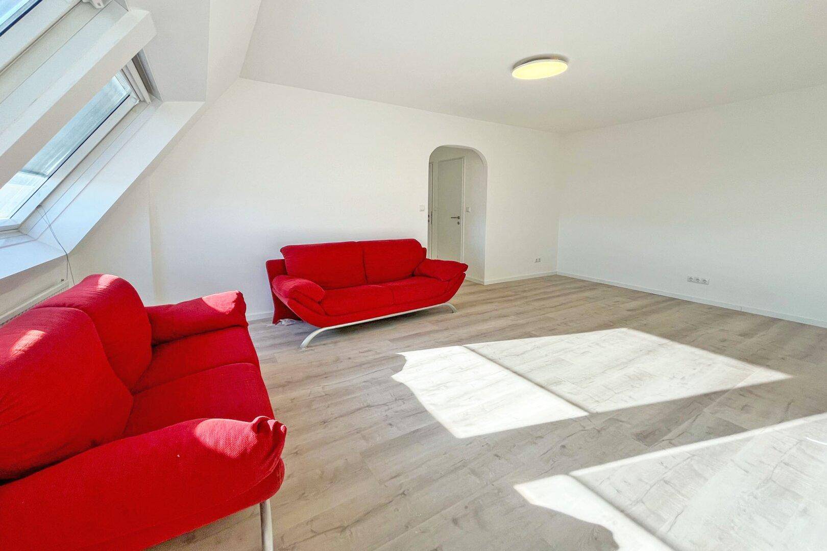 Geräumiges Wohnzimmer im Dachgeschoss mit viel Tageslicht und hellem Laminatboden.