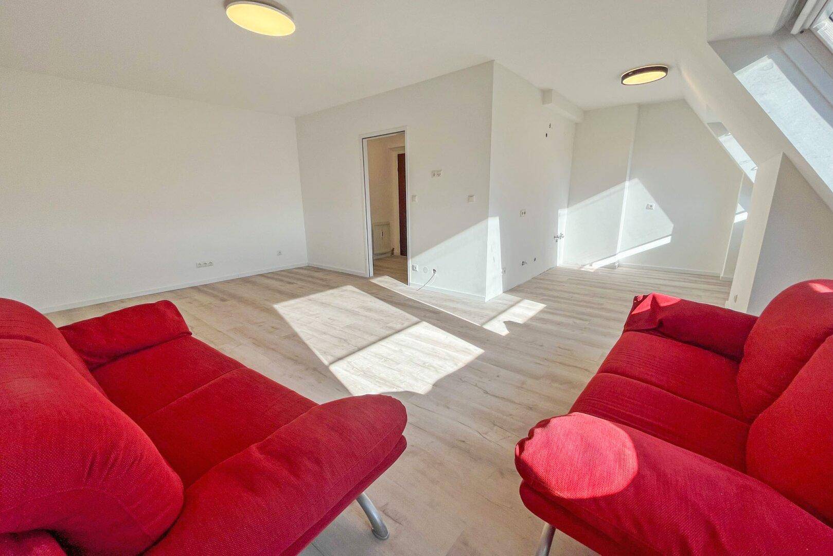 Heller Wohnbereich mit schrägen Wänden, Laminatboden und rotem Sofa im Dachgeschoss.