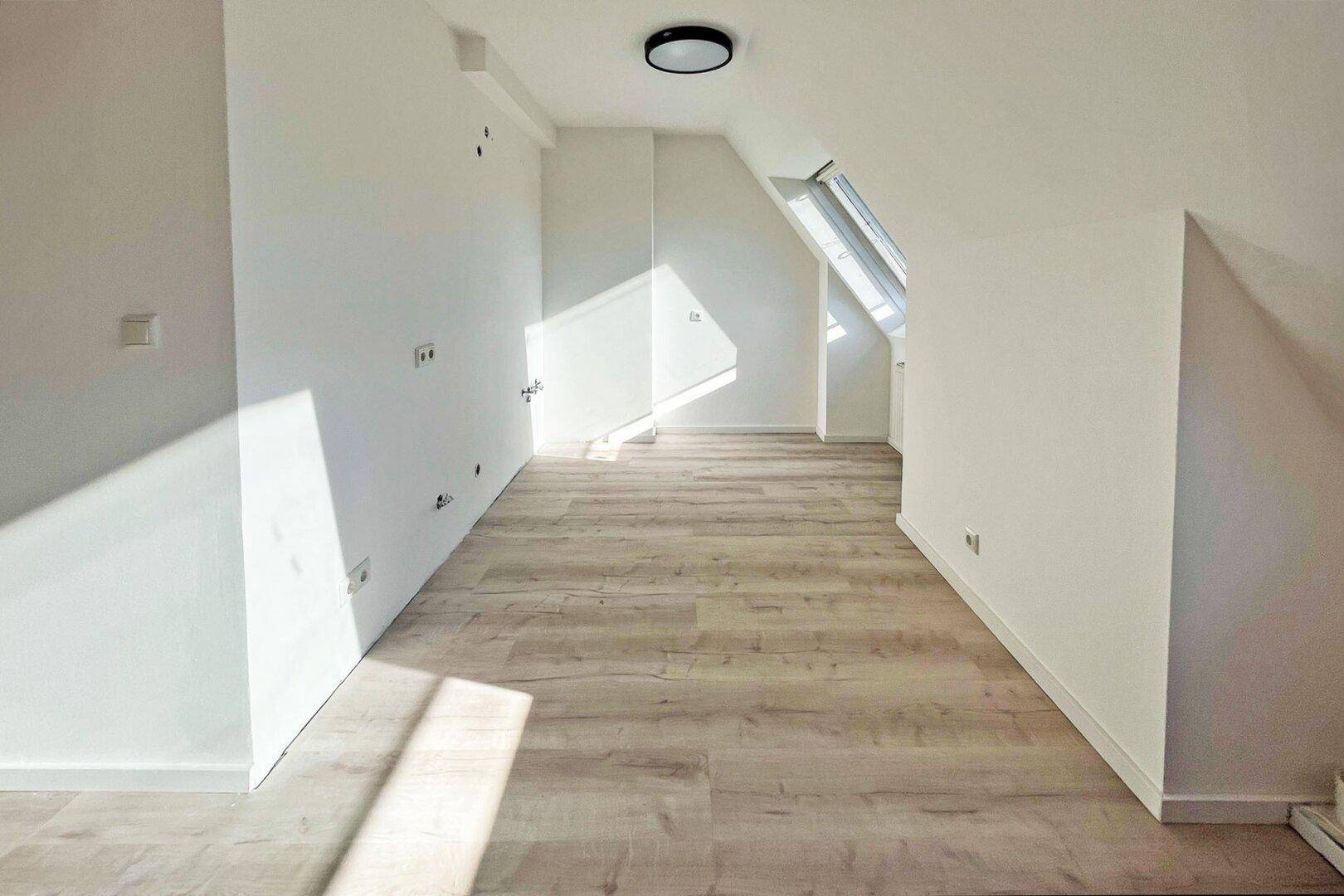 Leerer Raum im Dachgeschoss mit hellem Laminatboden und schrägen Wänden.