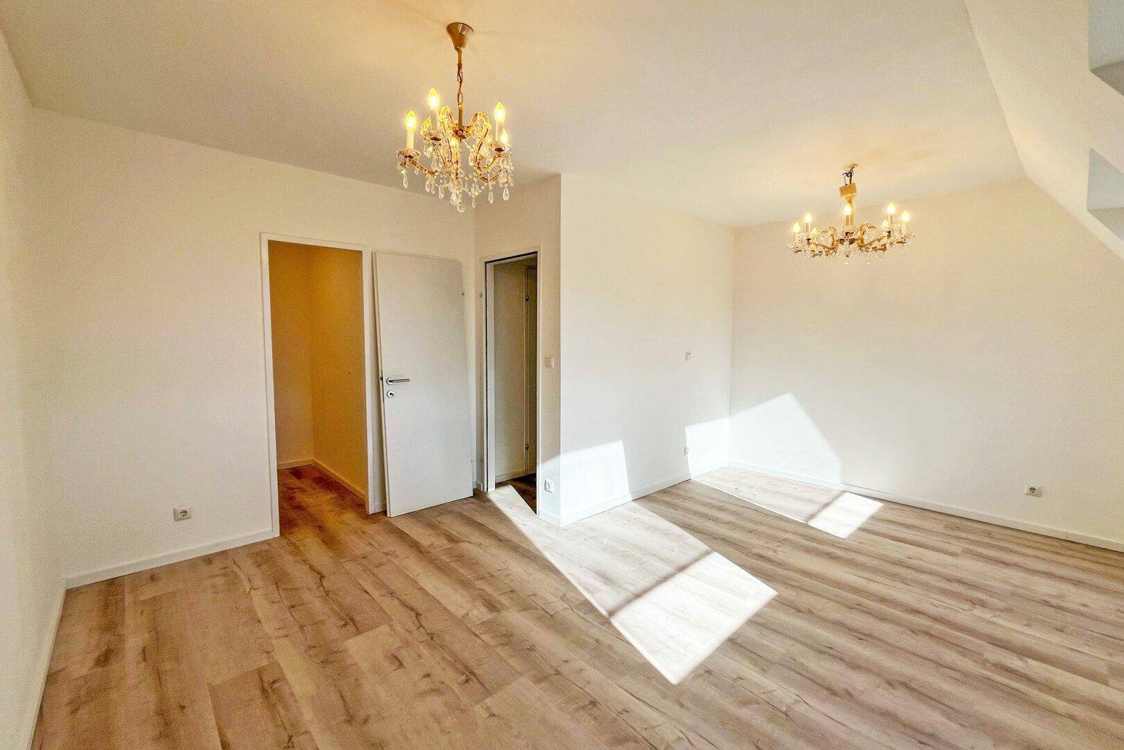 Heller Raum mit Laminatboden und zwei eleganten Kronleuchtern, ideal als Wohnbereich.