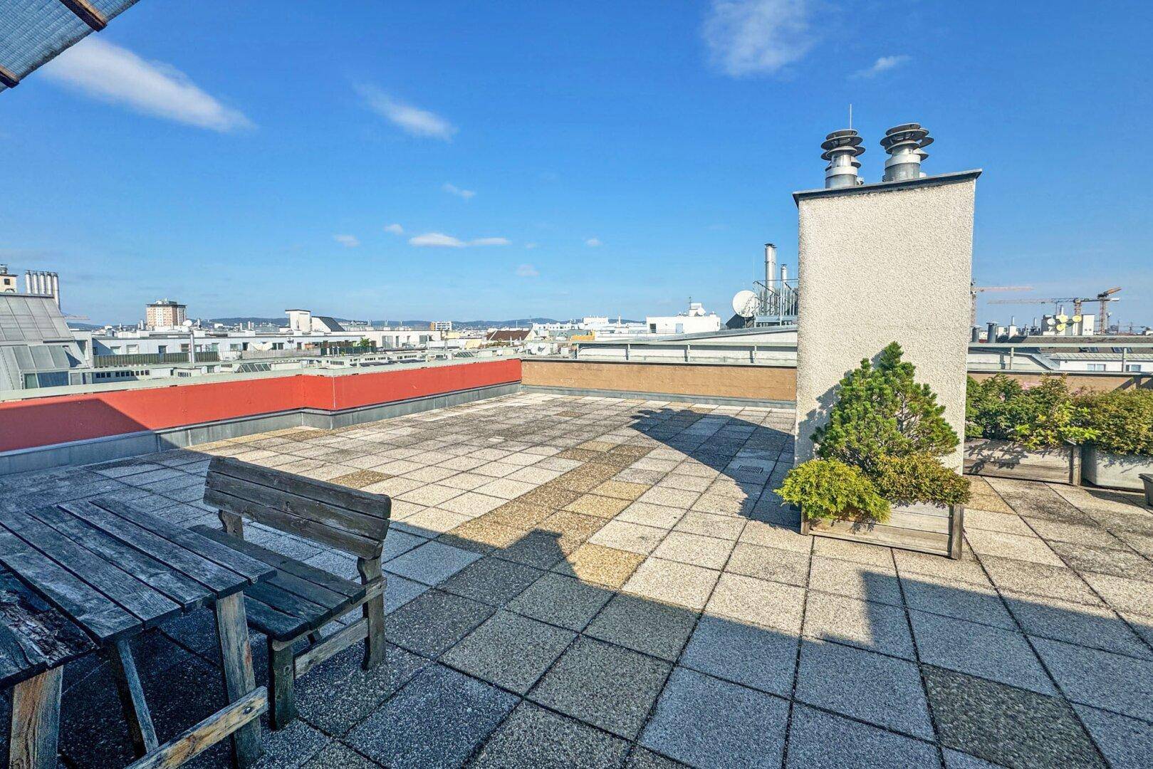 Große Dachterrasse mit Holztisch und Bank, bietet einen weiten Blick über die Stadt.