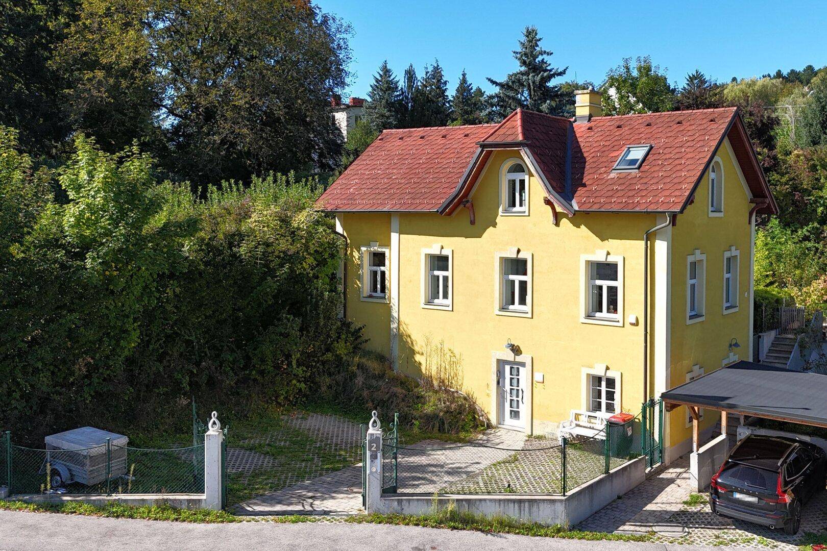 Vorderansicht des gelben Hauses mit rotem Dach, weißer Fassade und einem Carport.