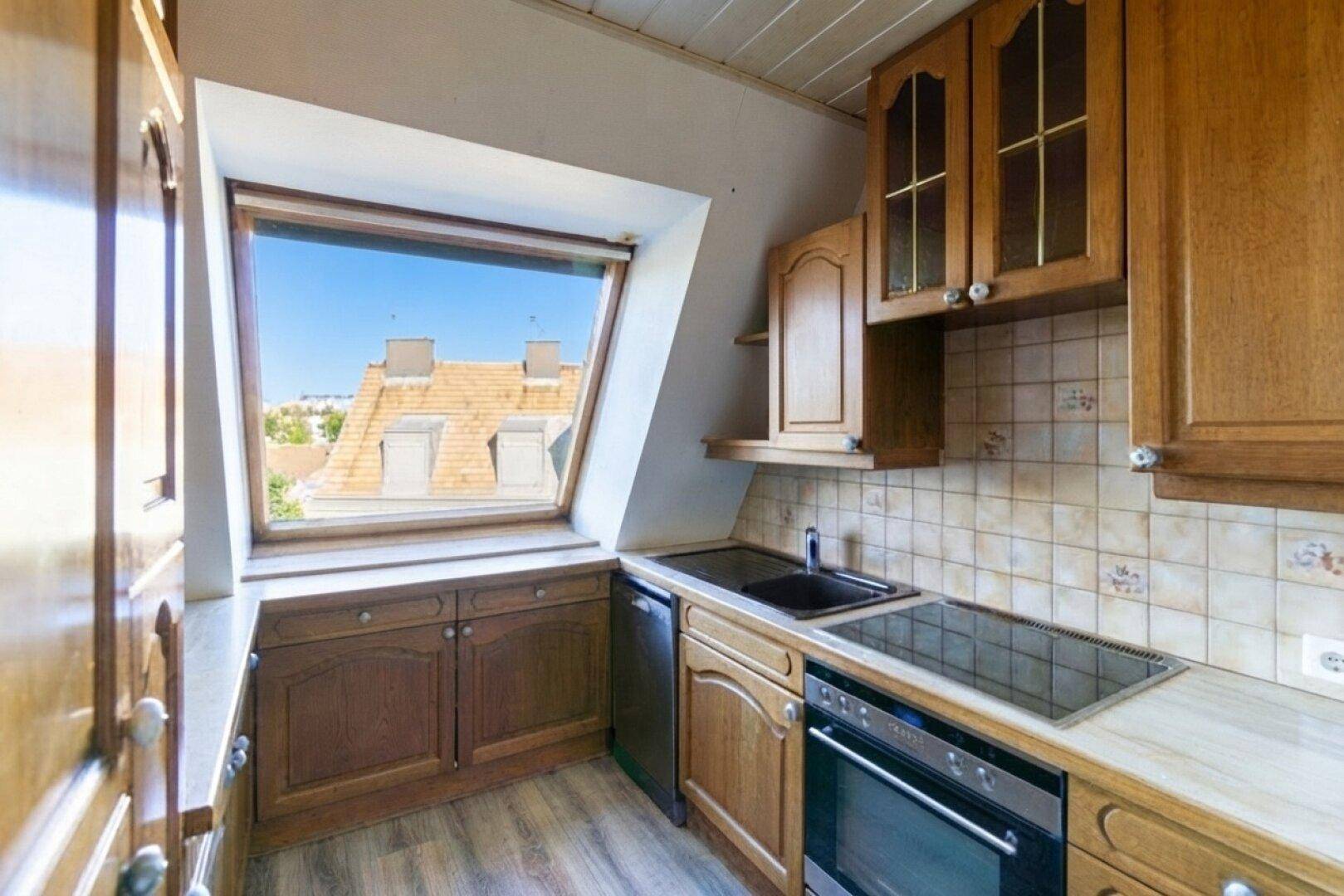 Kleine Küche im Dachgeschoss mit Holzschränken, Einbaugeräten und Dachfenster.