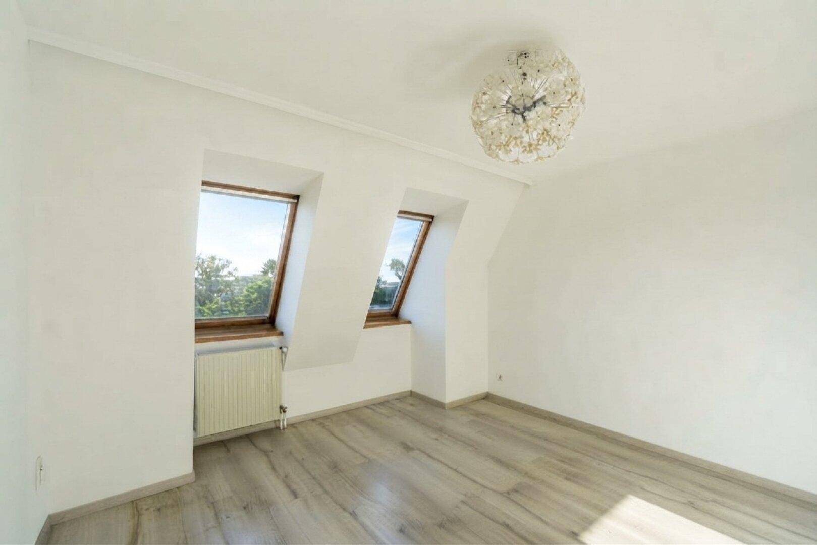Helles Zimmer im Dachgeschoss mit schrägen Wänden, Laminatboden und zwei Dachfenstern.