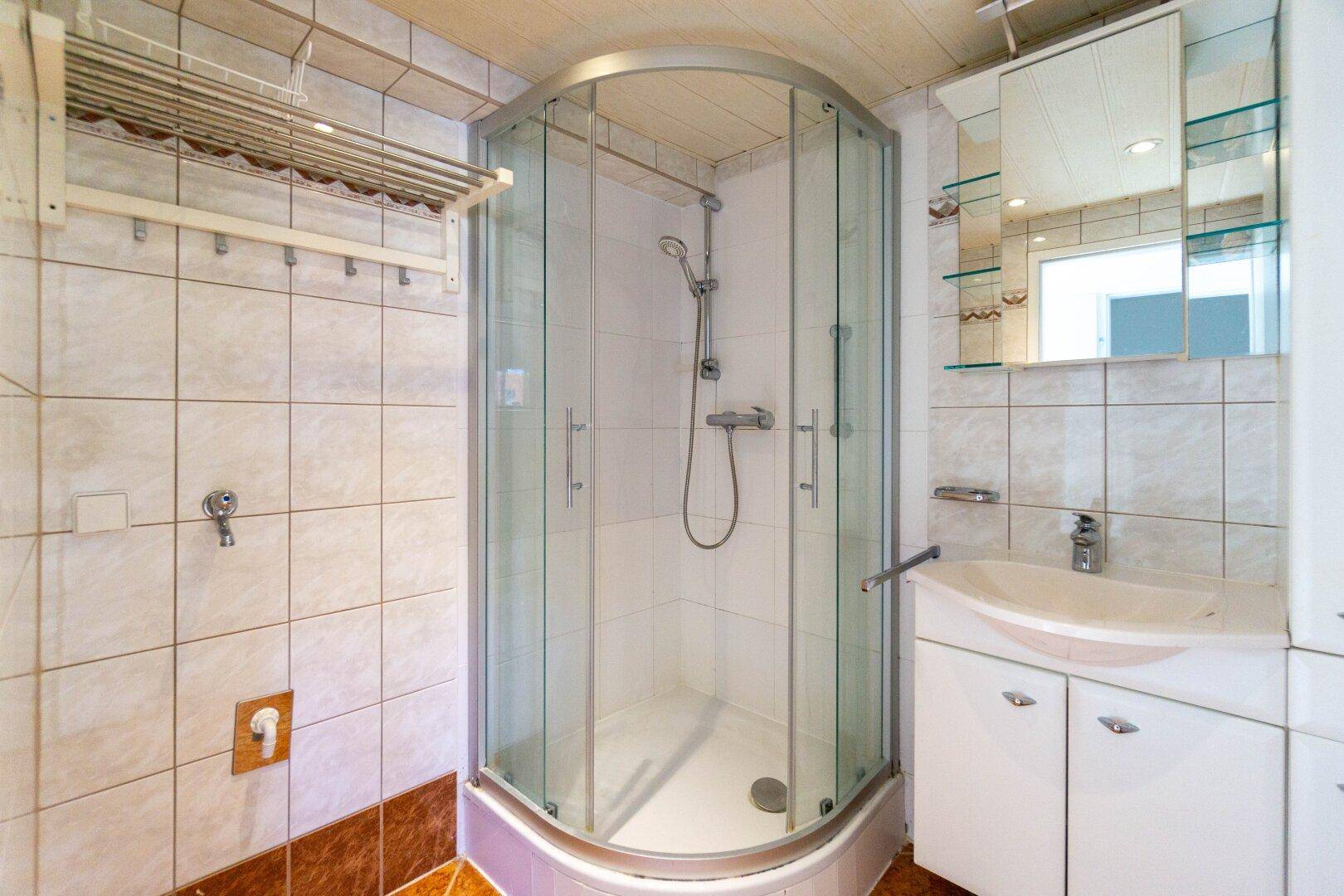 Gefliestes Badezimmer mit Duschkabine, Waschbecken und Spiegelschrank.