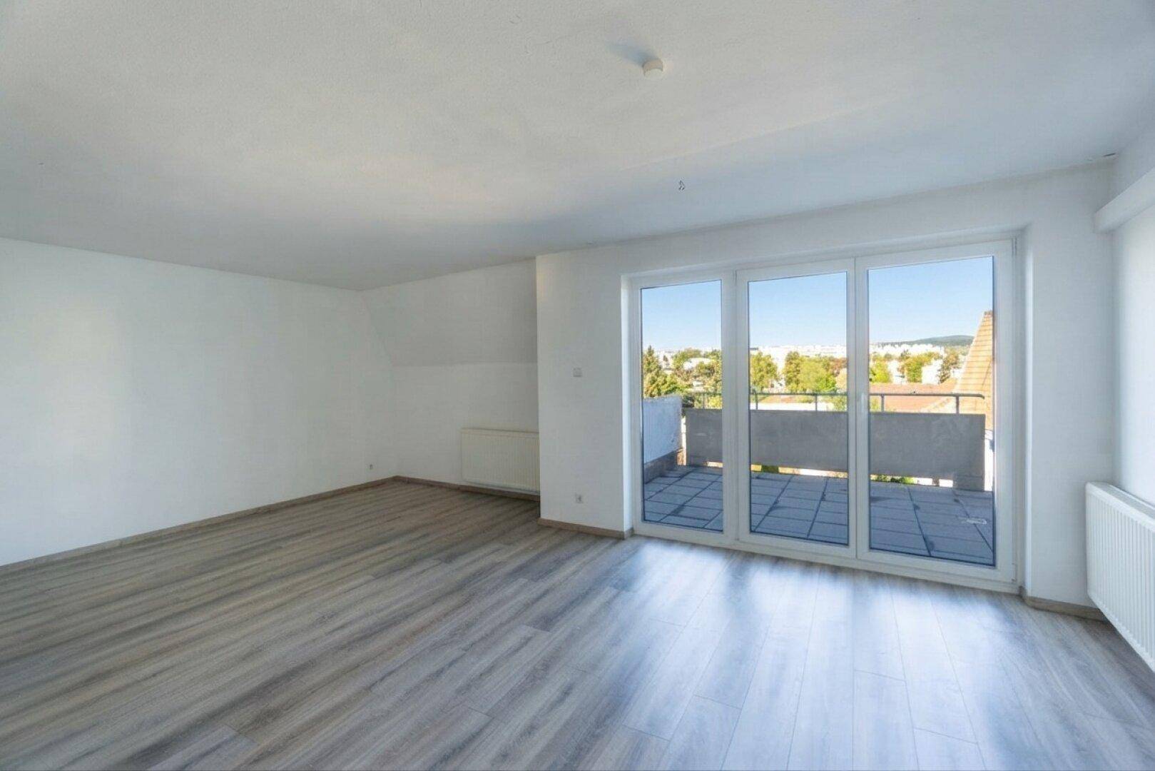 Helles, leeres Zimmer mit Laminatboden und großem Fenster mit Zugang zu einem Balkon.