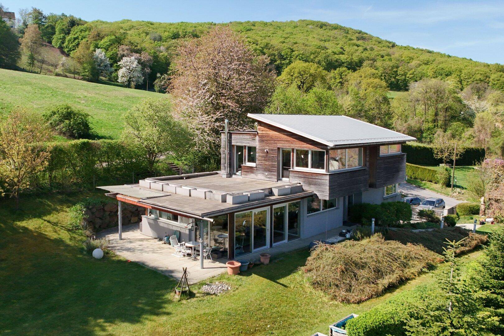 Modernes Einfamilienhaus mit Holzfassade, großer Terrasse und weitläufigem Garten in Hanglage.