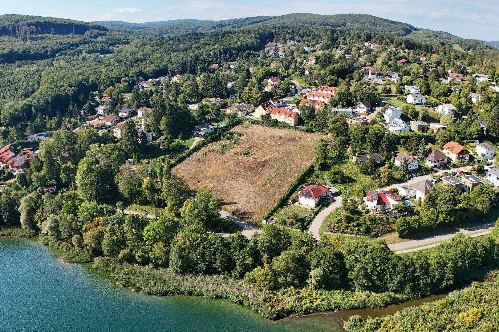 Panoramablick auf einen See, bewaldete Hügel und ein großes Grundstück mit angrenzenden Häusern.