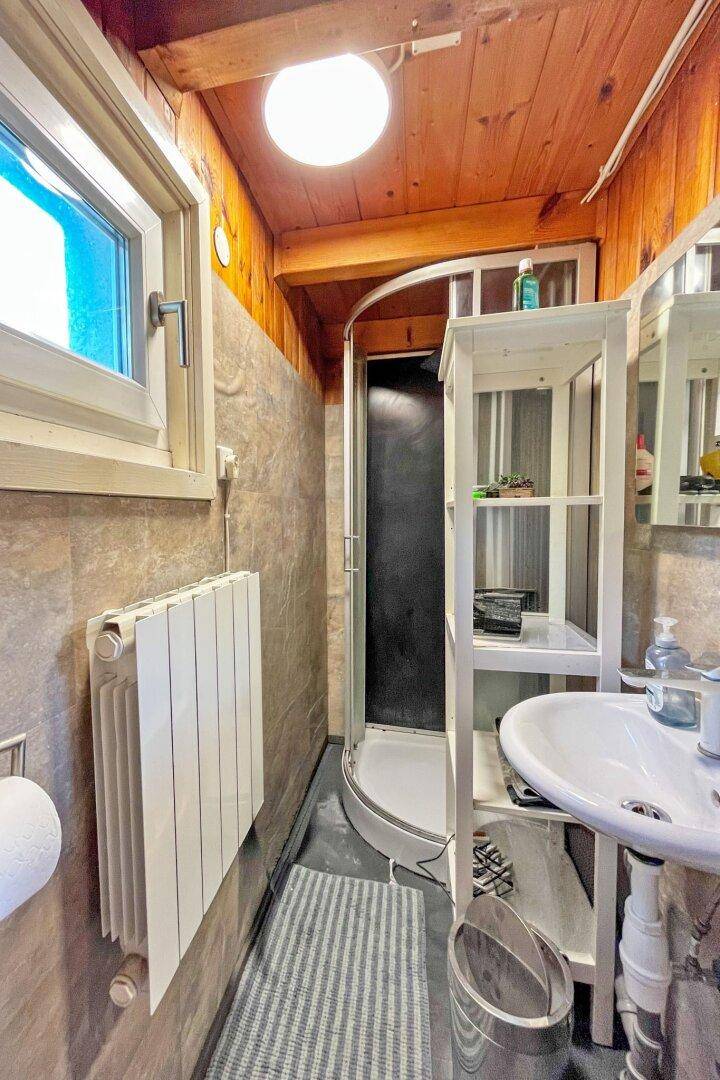 Kleines Badezimmer mit Duschkabine, Waschbecken, Heizkörper und Fenster.