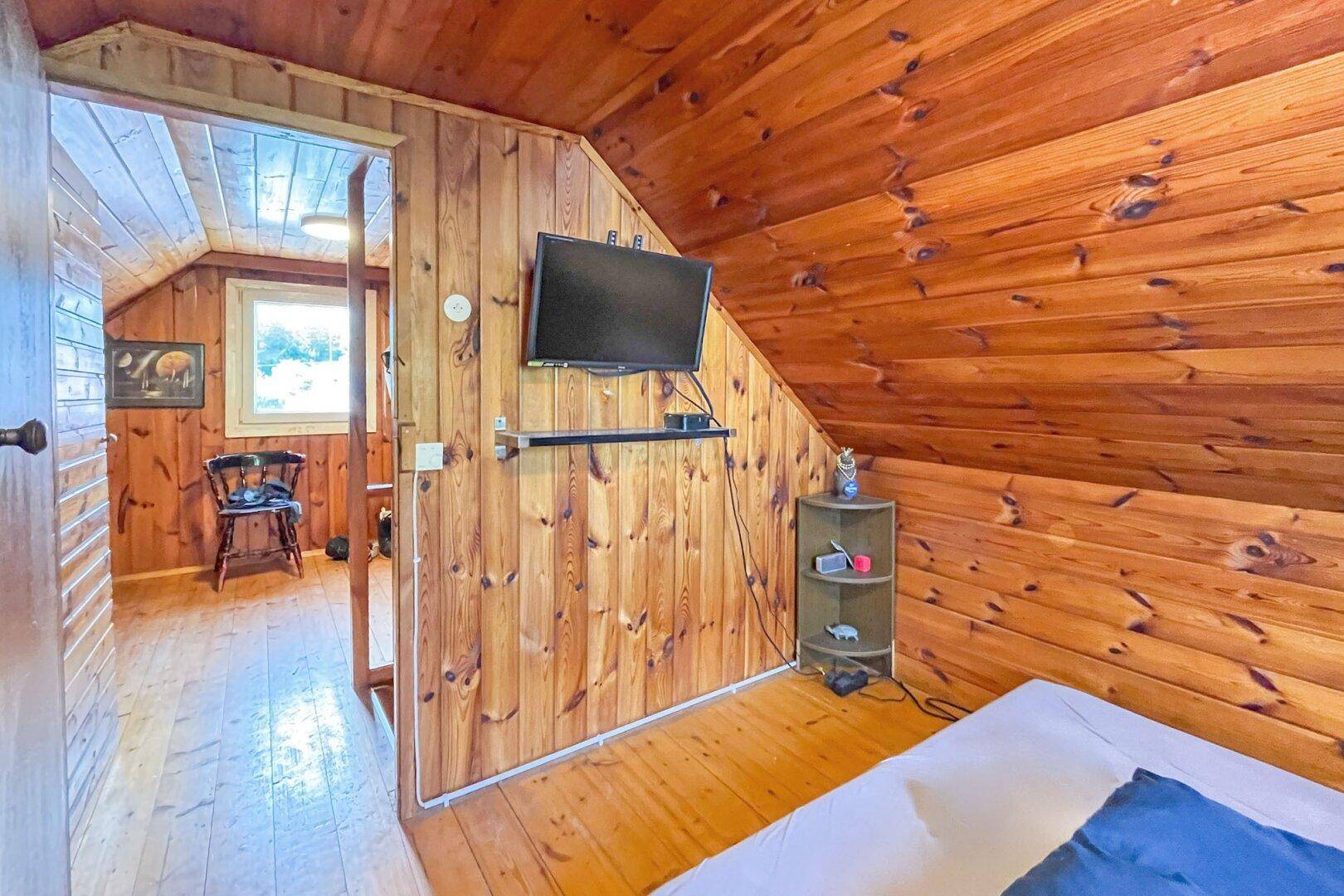 Dachgeschoss-Schlafzimmer mit Holzwänden, Fernseher und gemütlichem Bettbereich.