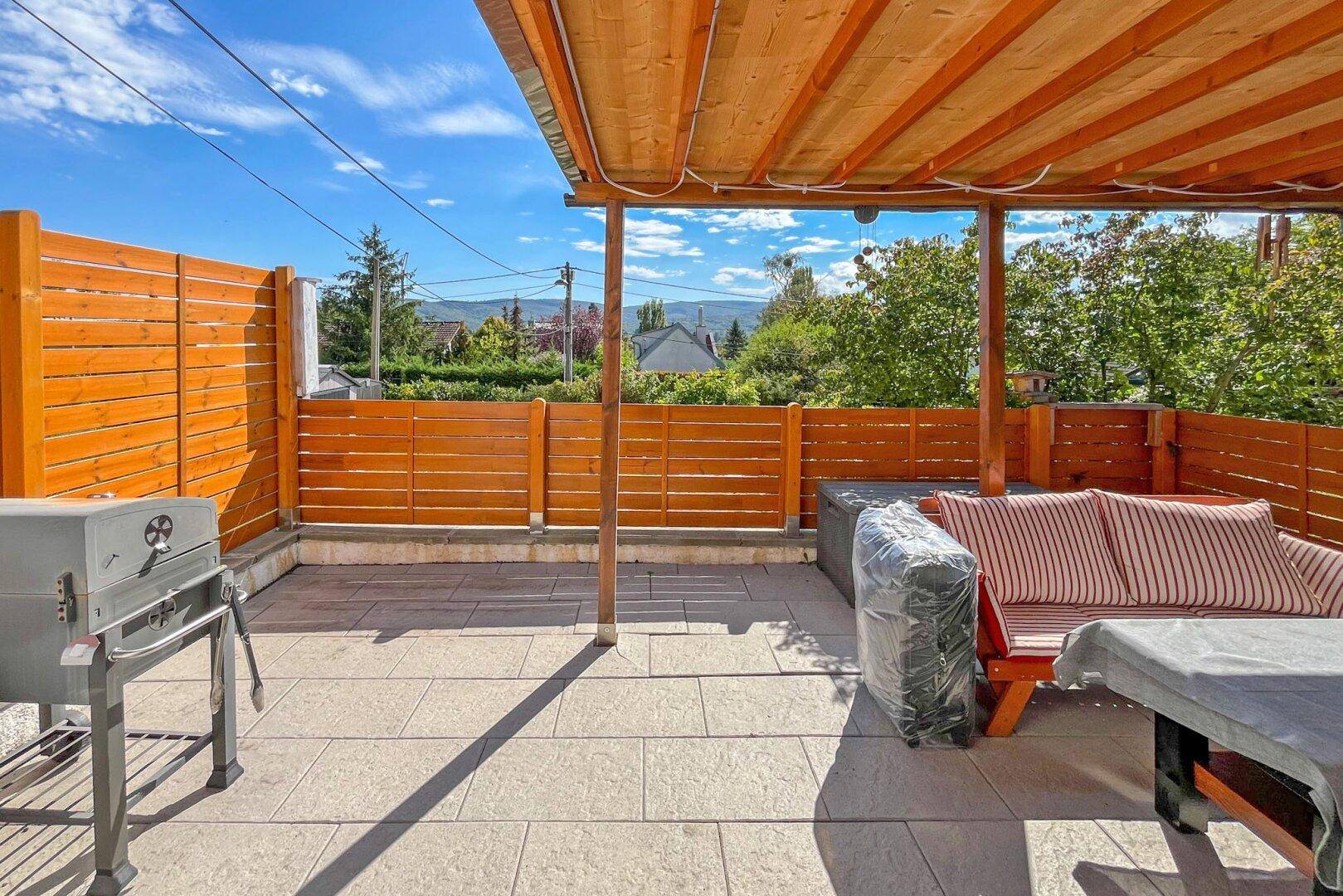 Überdachte Terrasse mit Holzverkleidung, Sitzgelegenheiten und Grillbereich.