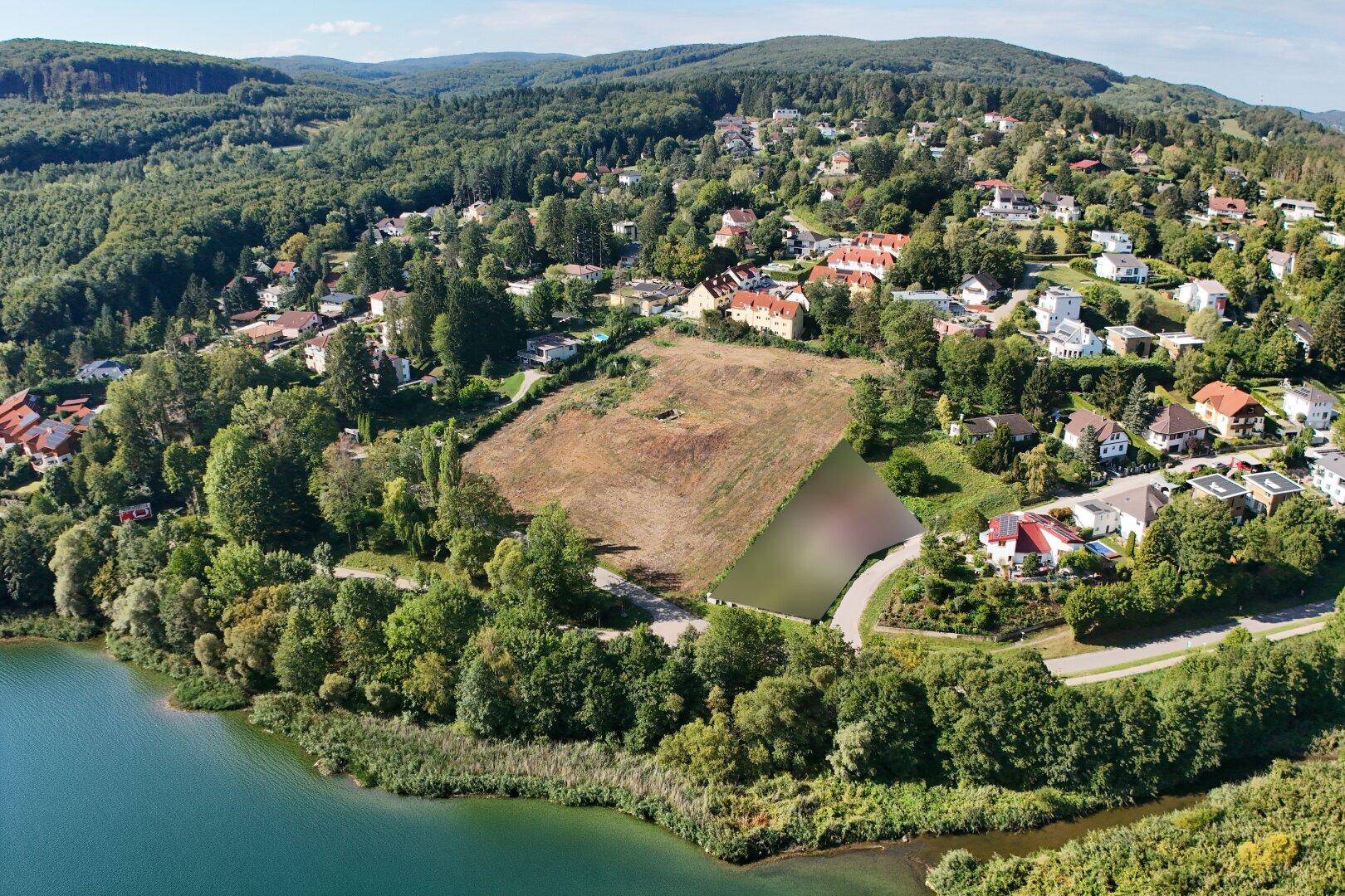 Luftaufnahme eines großen Grundstücks mit Seezugang, umgeben von Wald und Wohngebäuden.