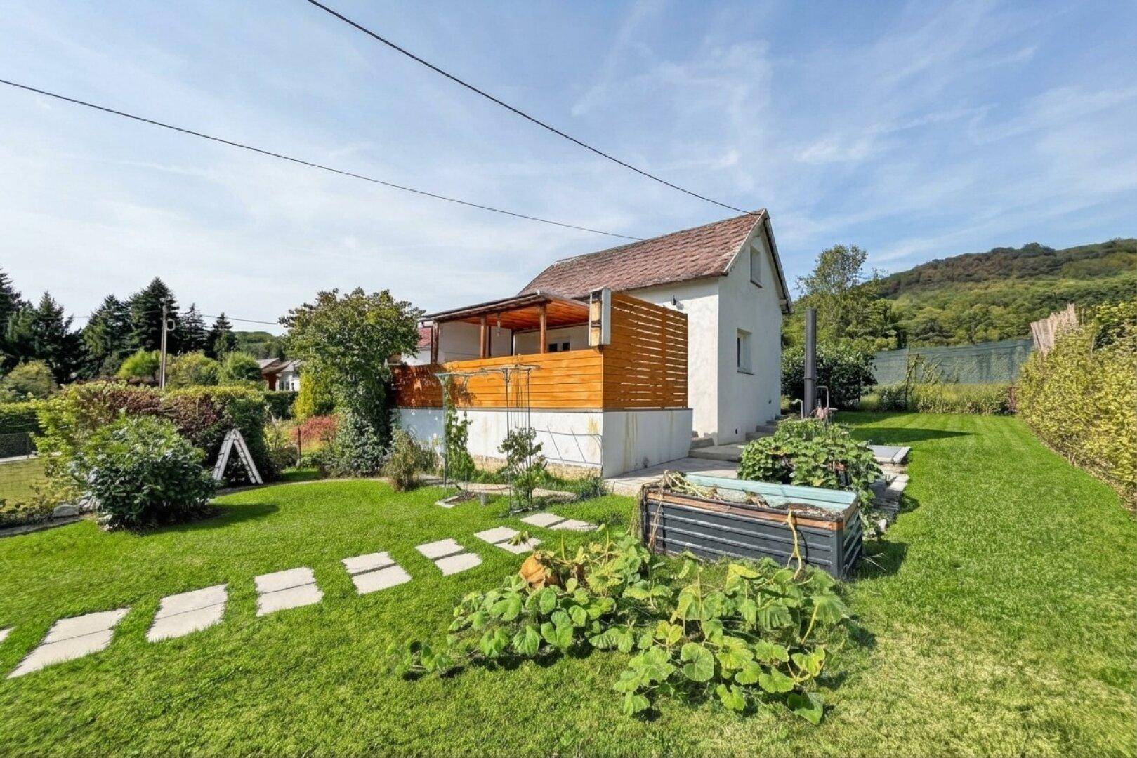 Haus mit Holzterrasse und großem Gartenbereich mit Rasen und Pflanzenbeeten.