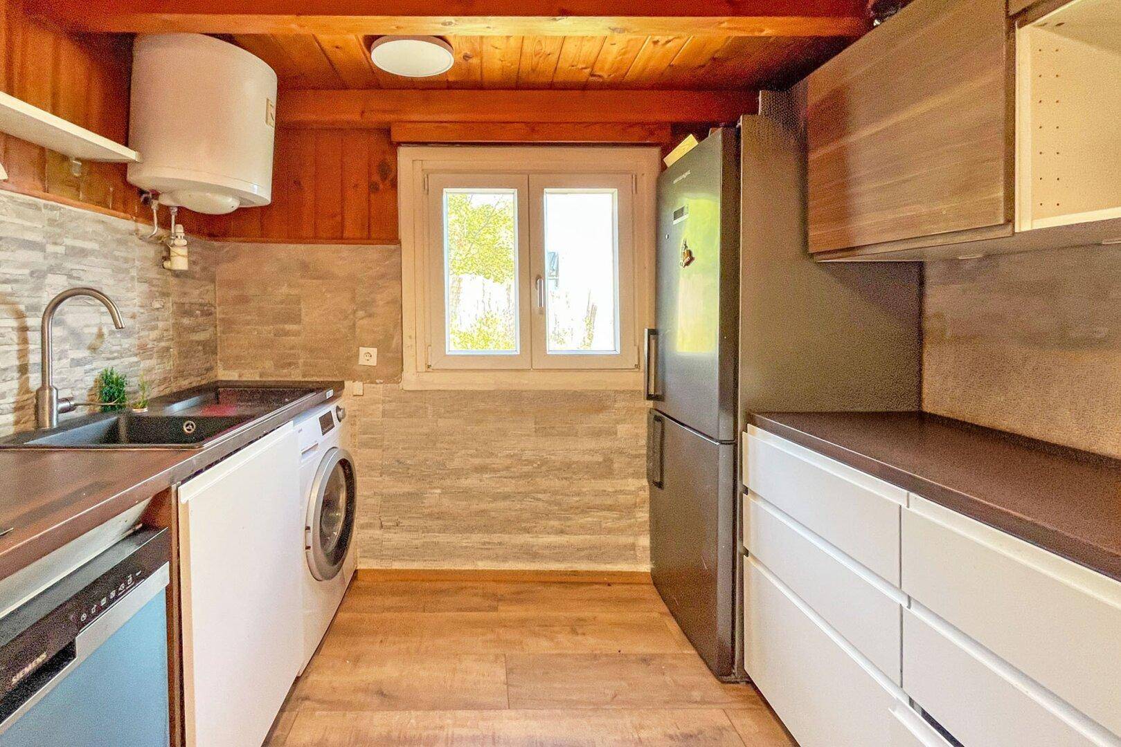 Funktionale Küchenzeile mit Spüle, Waschmaschine und Kühlschrank unter Holzdecke.