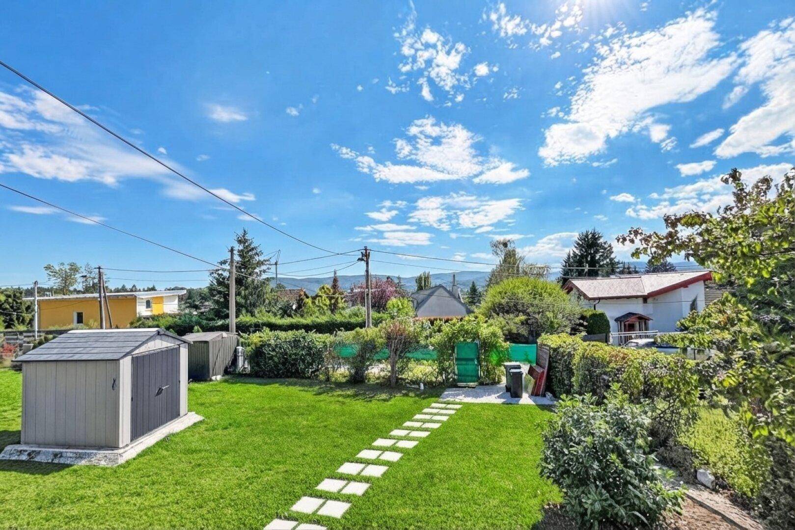 Sonniger Garten mit Rasenfläche, Gartenhaus und Blick auf die umliegende Landschaft.