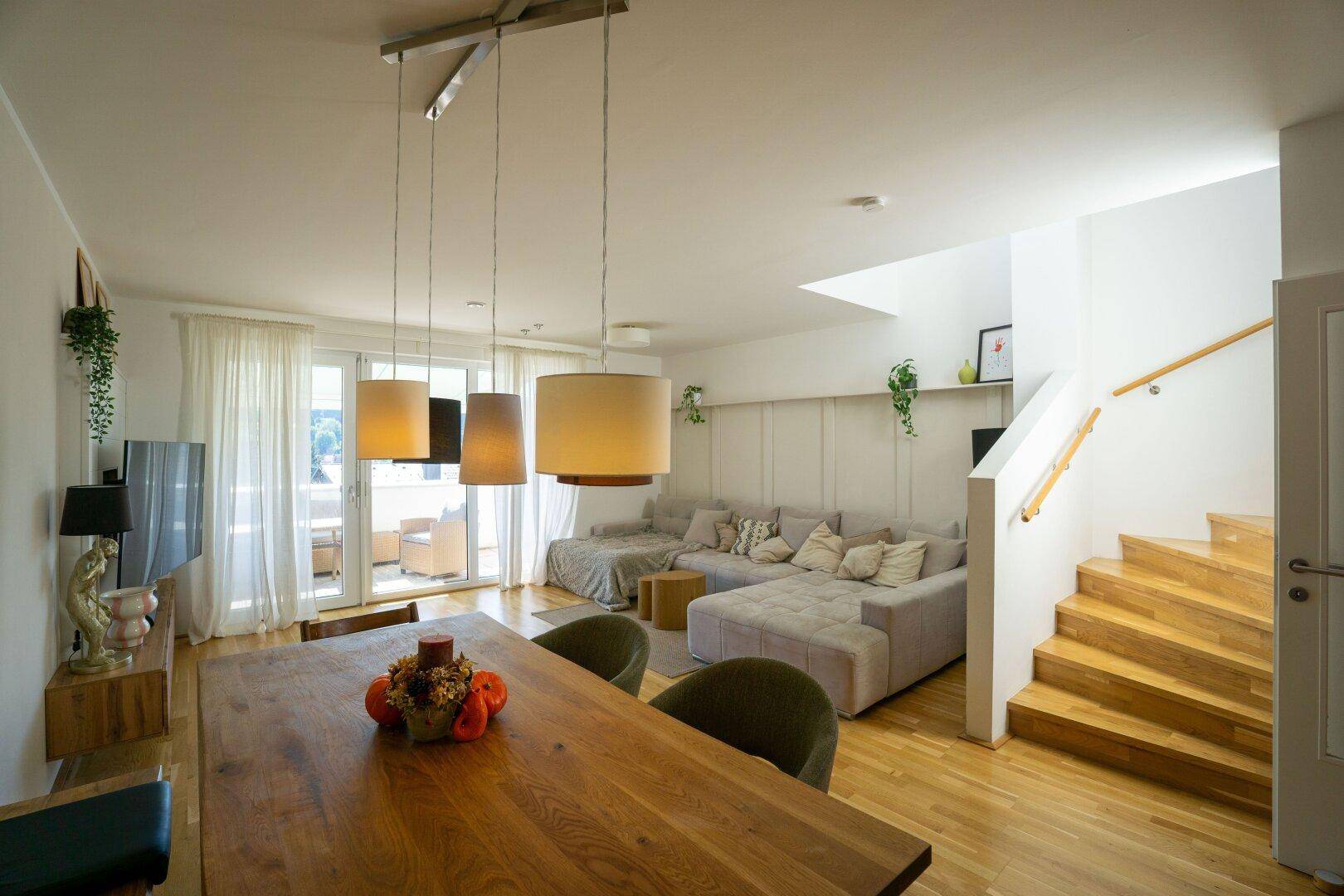 Offener Wohn- und Essbereich mit Holzboden, bequemer Couch und Zugang zum Balkon.