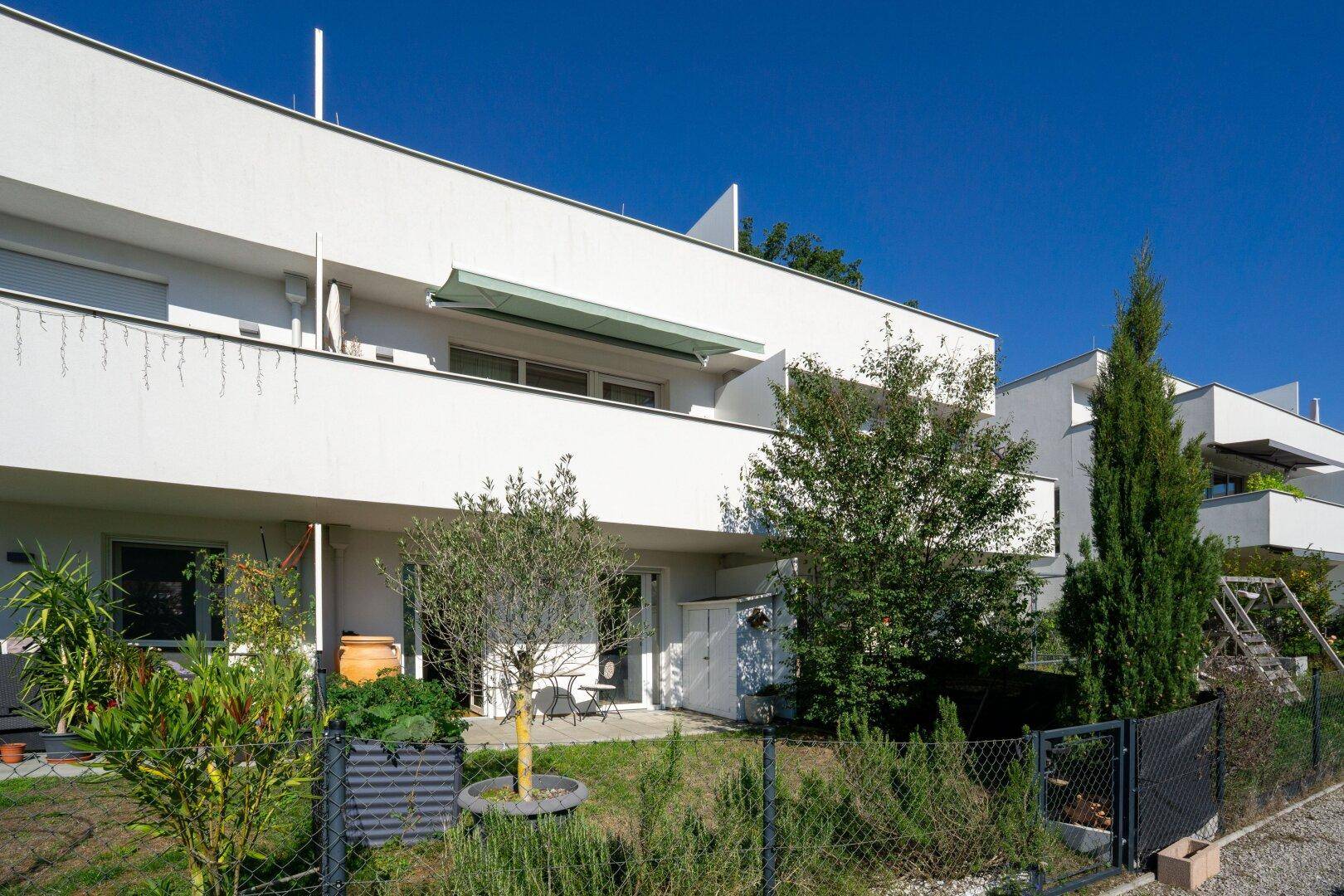 Moderne Gebäudefassade mit Balkonen und einem kleinen, gepflegten Gartenbereich im Vordergrund.