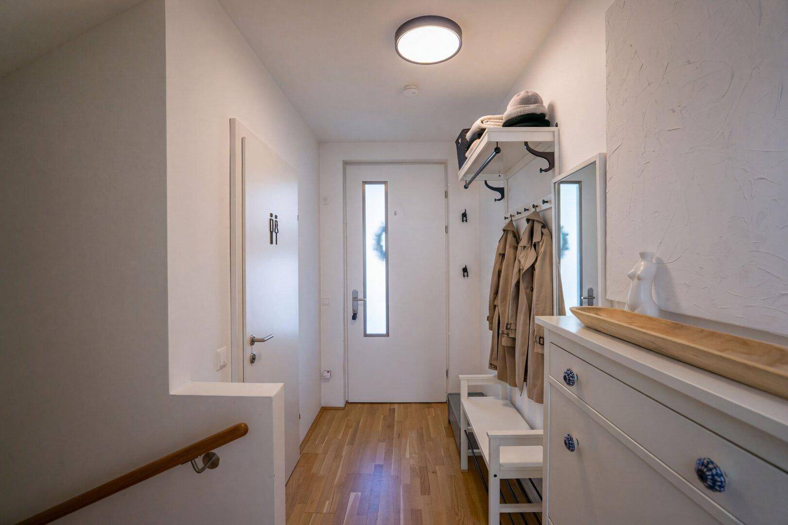 Heller Eingangsbereich mit Garderobe, Spiegel und praktischer Schuhkommode.