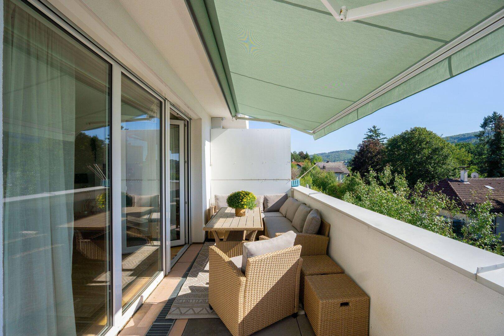 Heller Balkon mit Markise, Sitzgelegenheiten und Blick ins Grüne.