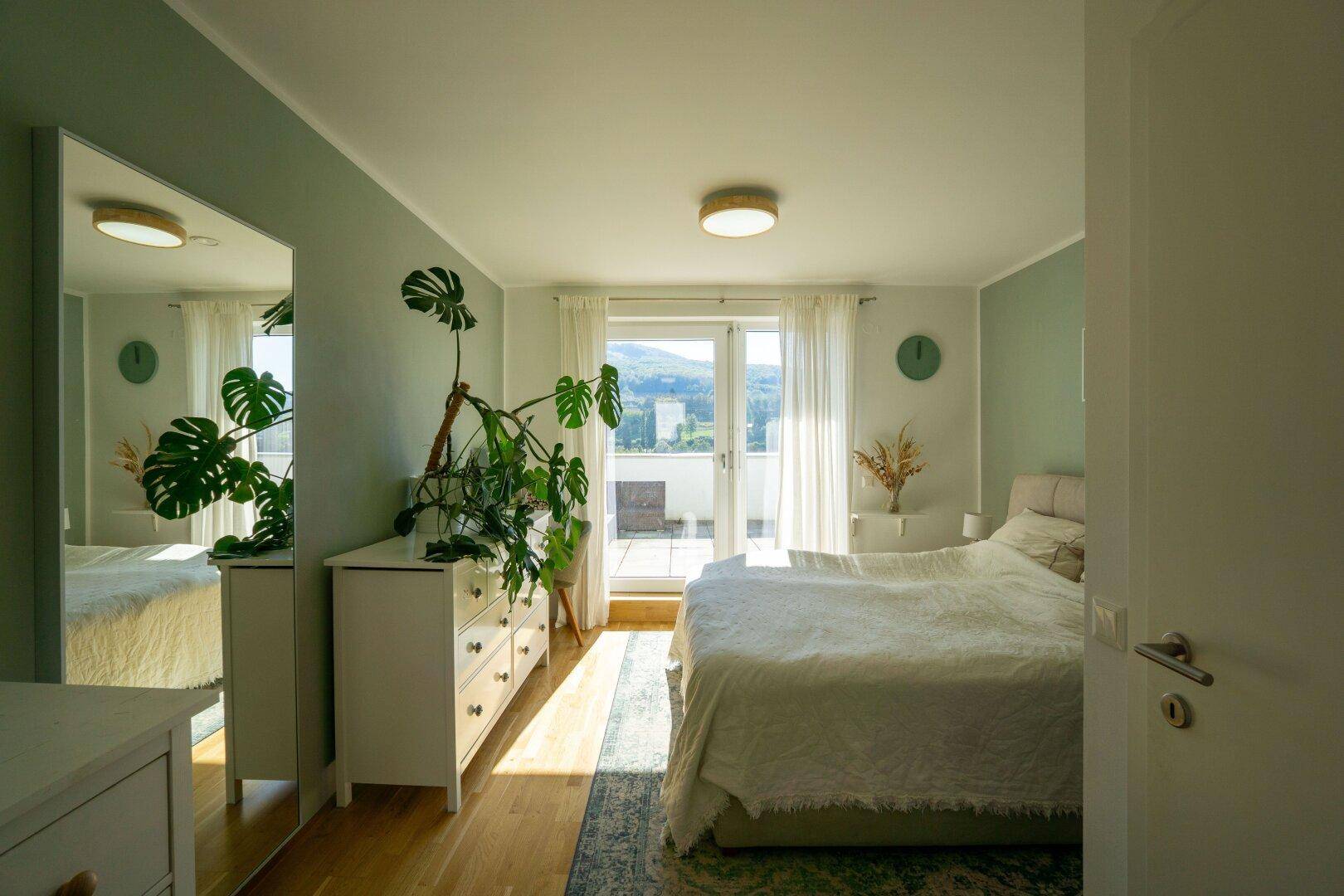 Helles Schlafzimmer mit Holzboden, großem Fenster und Zugang zu einem Außenbereich.
