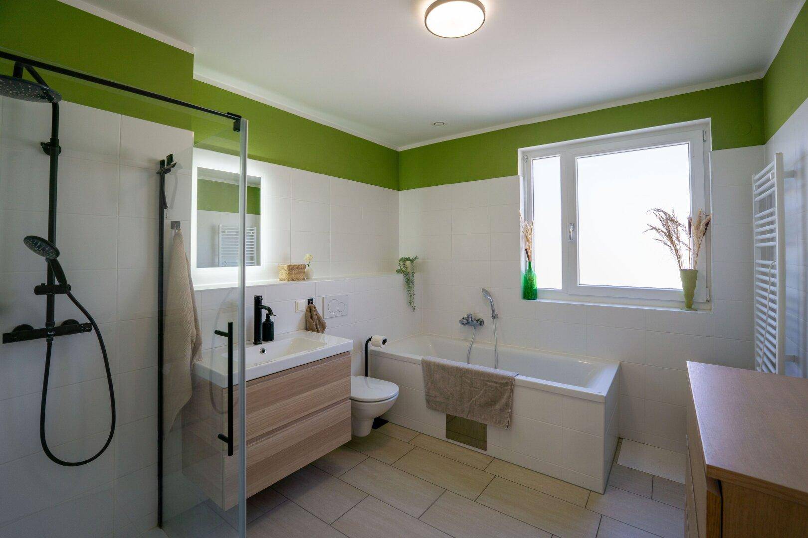 Modernes Badezimmer mit grünen Akzentwänden, Badewanne, Dusche und Fenster.