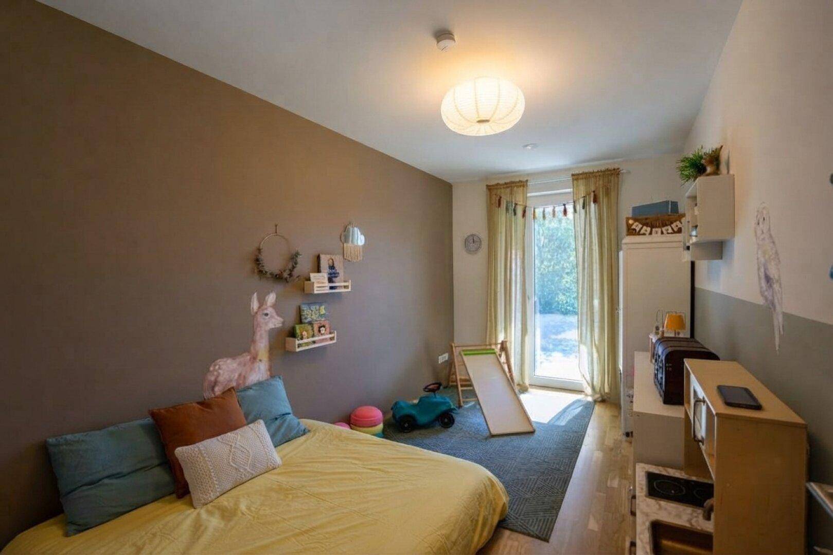 Freundliches Kinderzimmer mit Holzboden, farbiger Wandgestaltung und Zugang zum Garten.