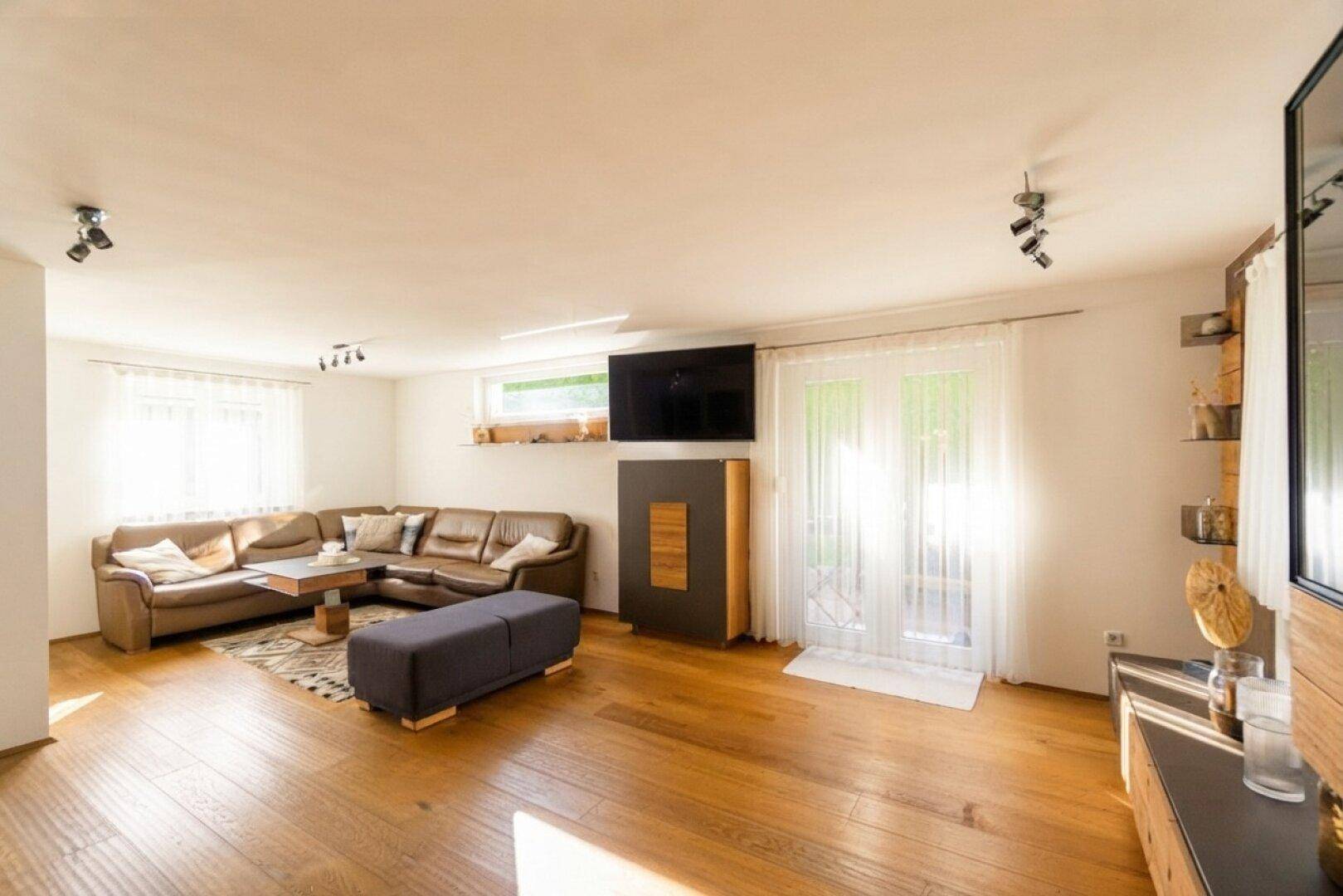 Helles Wohnzimmer mit bequemer Ledercouch, Holzboden und Zugang zum Außenbereich.