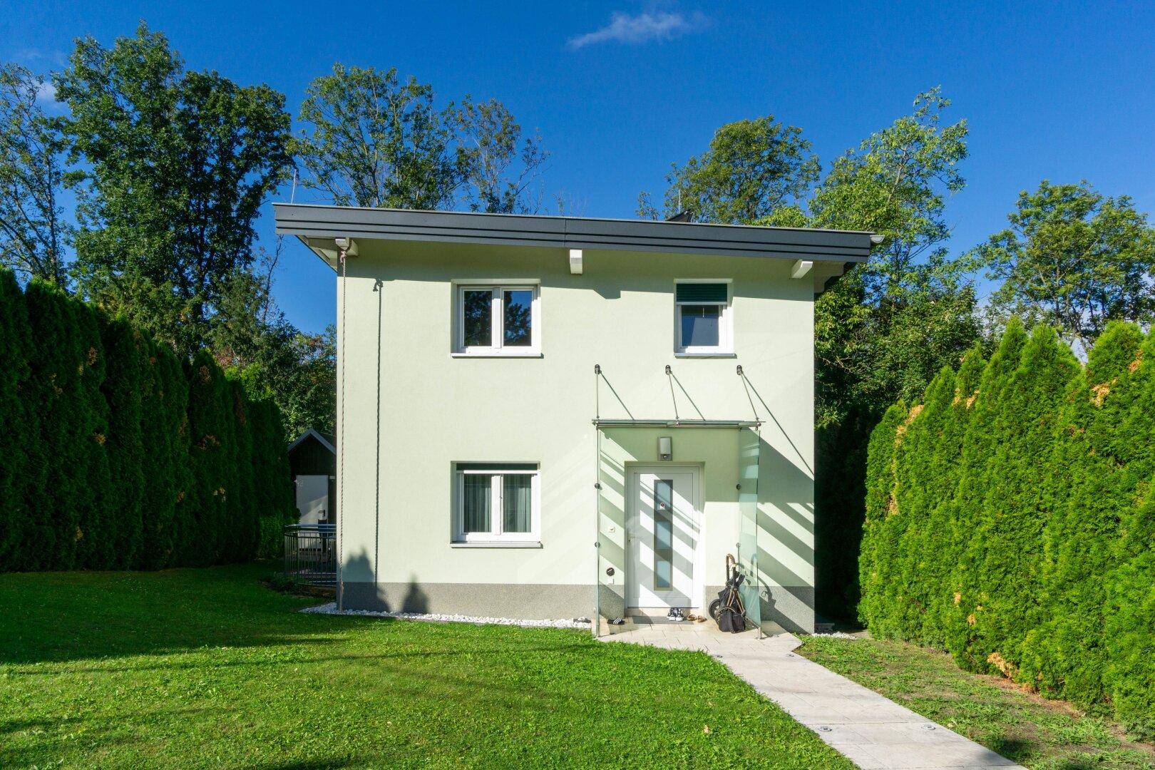 Modernes Einfamilienhaus mit hellgrüner Fassade, Vorgarten und klarem Design.