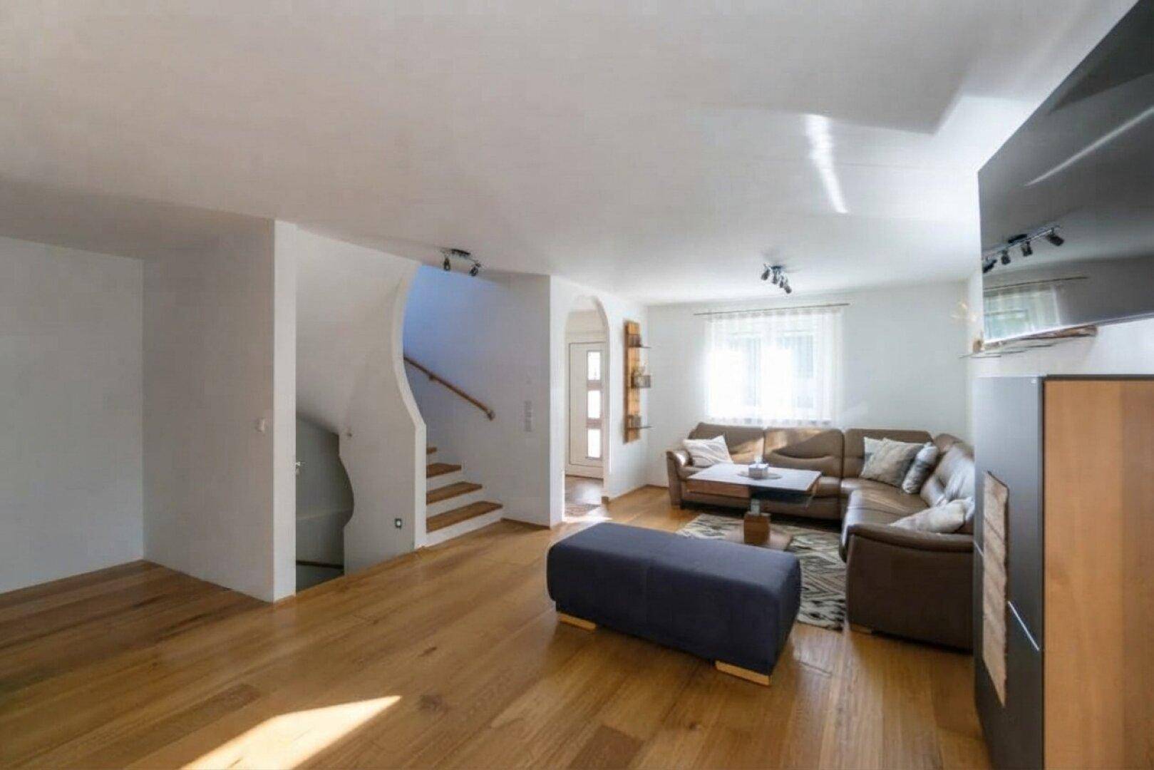 Geräumiges Wohnzimmer mit Holzboden, Ledersofa und offener Treppe zum Obergeschoss.