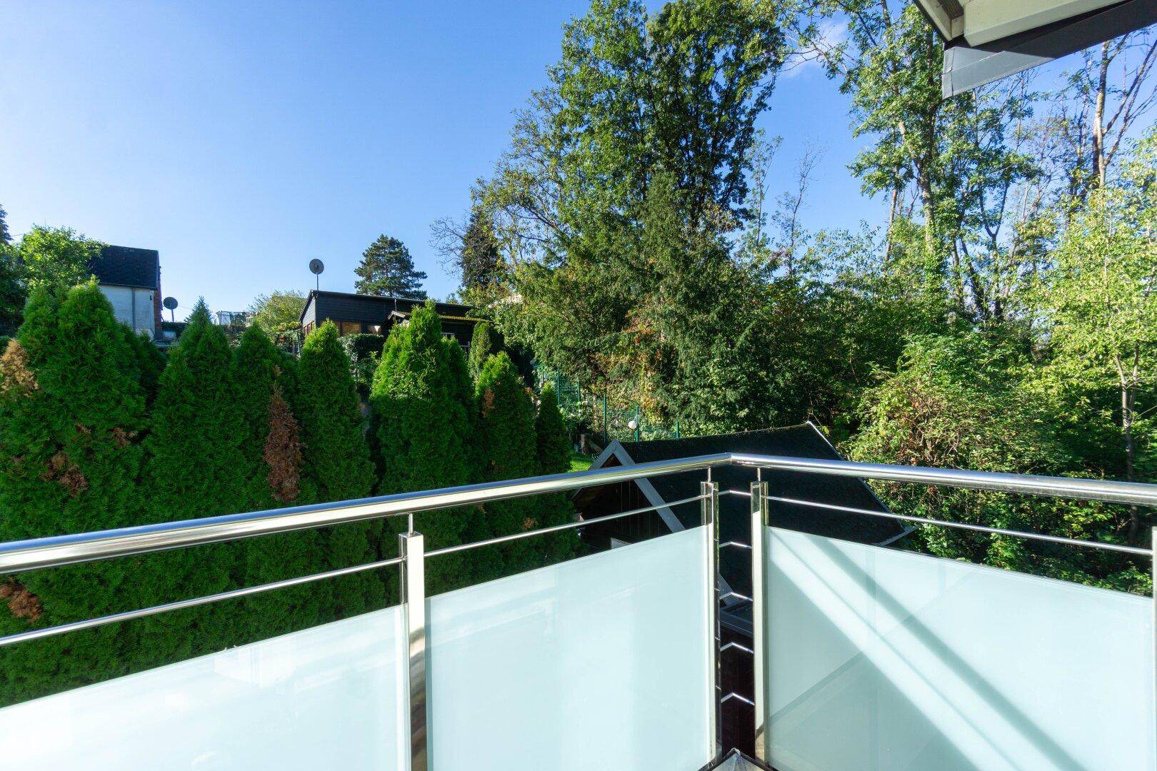 Moderner Balkon mit Glasbrüstung und Blick ins Grüne sowie auf die Nachbarschaft.