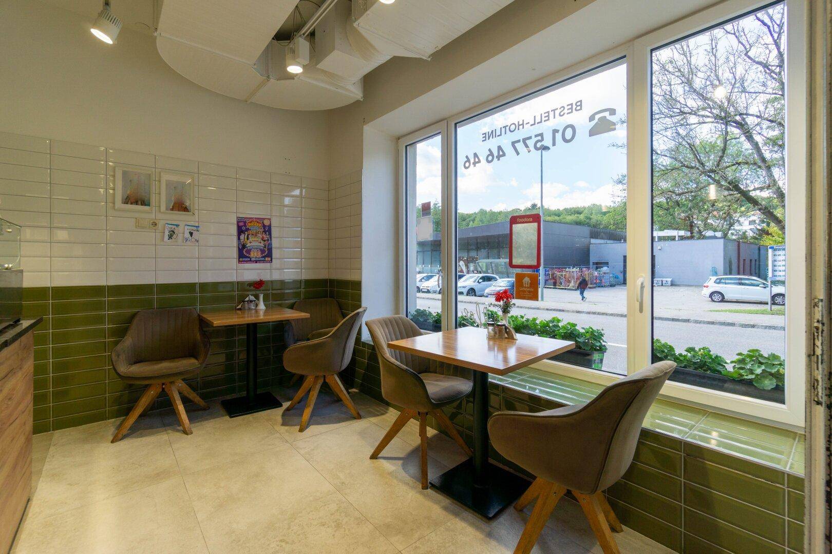 Heller Essbereich eines Restaurants mit modernen Stühlen, Holztischen und großen Fenstern zur Straße.
