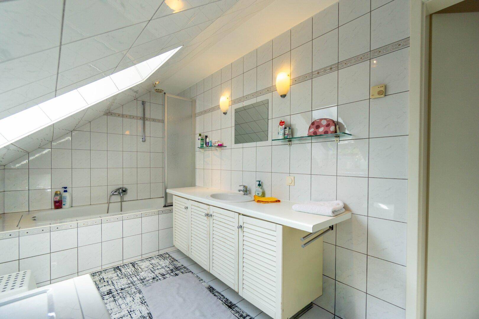 Gefliestes Badezimmer unter Dachschrägen mit Badewanne, Dusche und Dachfenster für natürliches Licht.