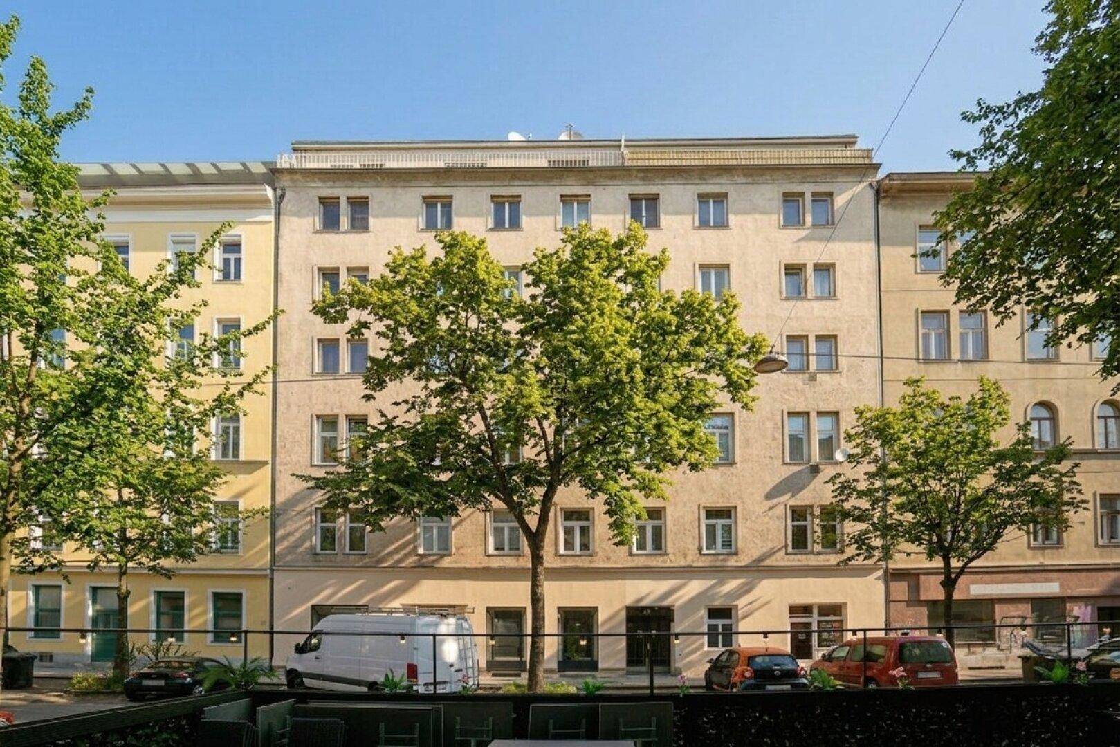 Fassade eines klassischen Mehrfamilienhauses mit vielen Fenstern und Bäumen davor.