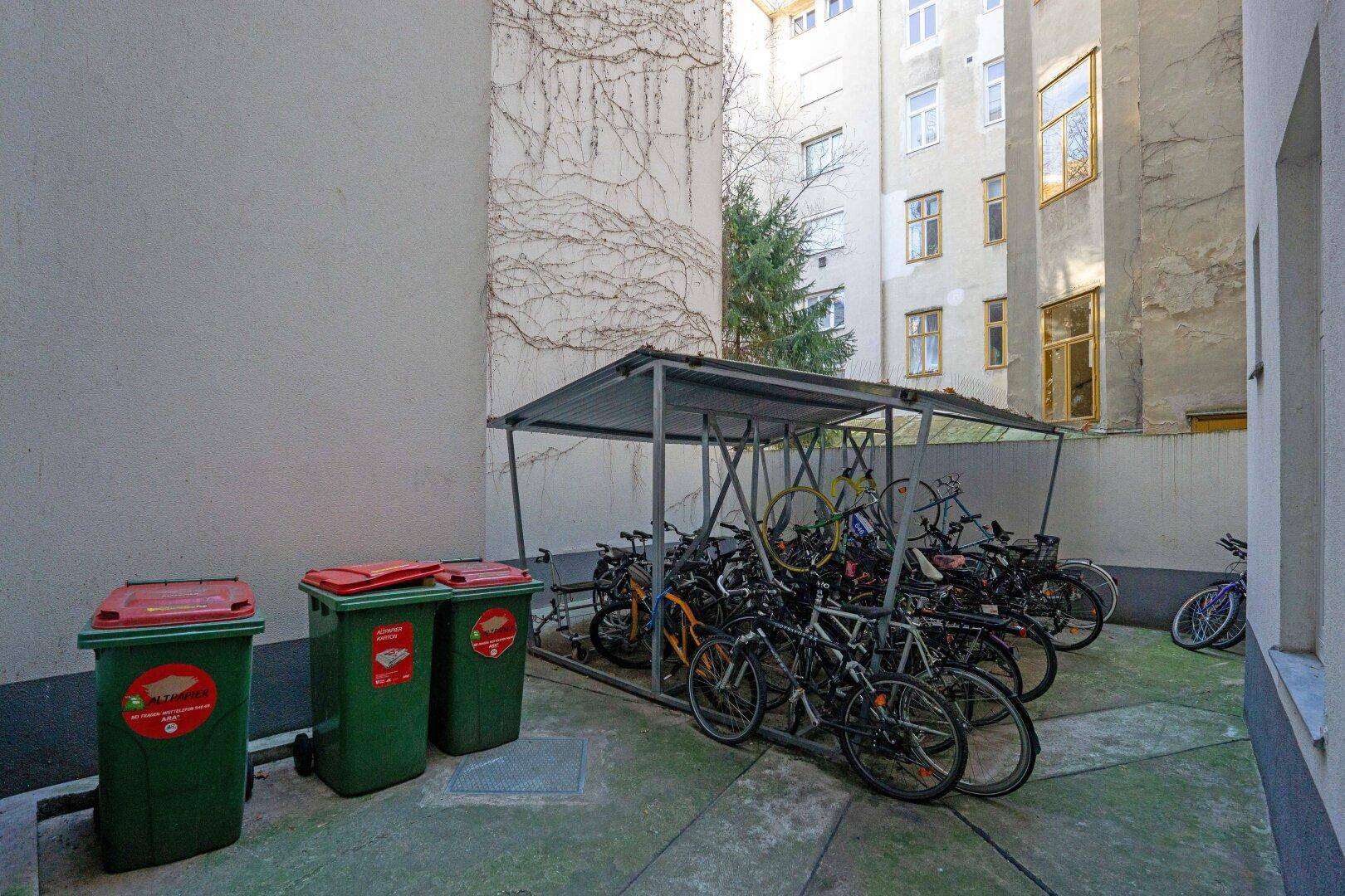 Überdachter Fahrradabstellplatz mit Mülltonnen in einem Hinterhofbereich des Gebäudes.