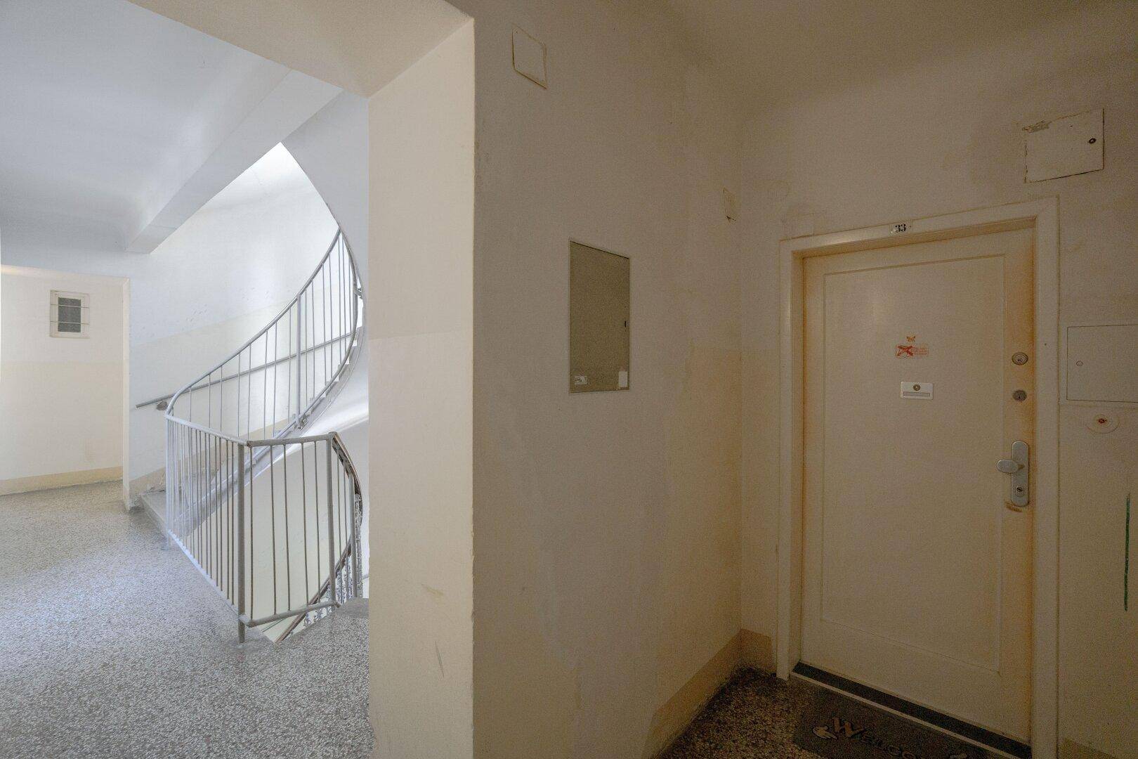 Treppenabsatz mit schlichtem Geländer und einer Wohnungstür in einem Mehrfamilienhaus.