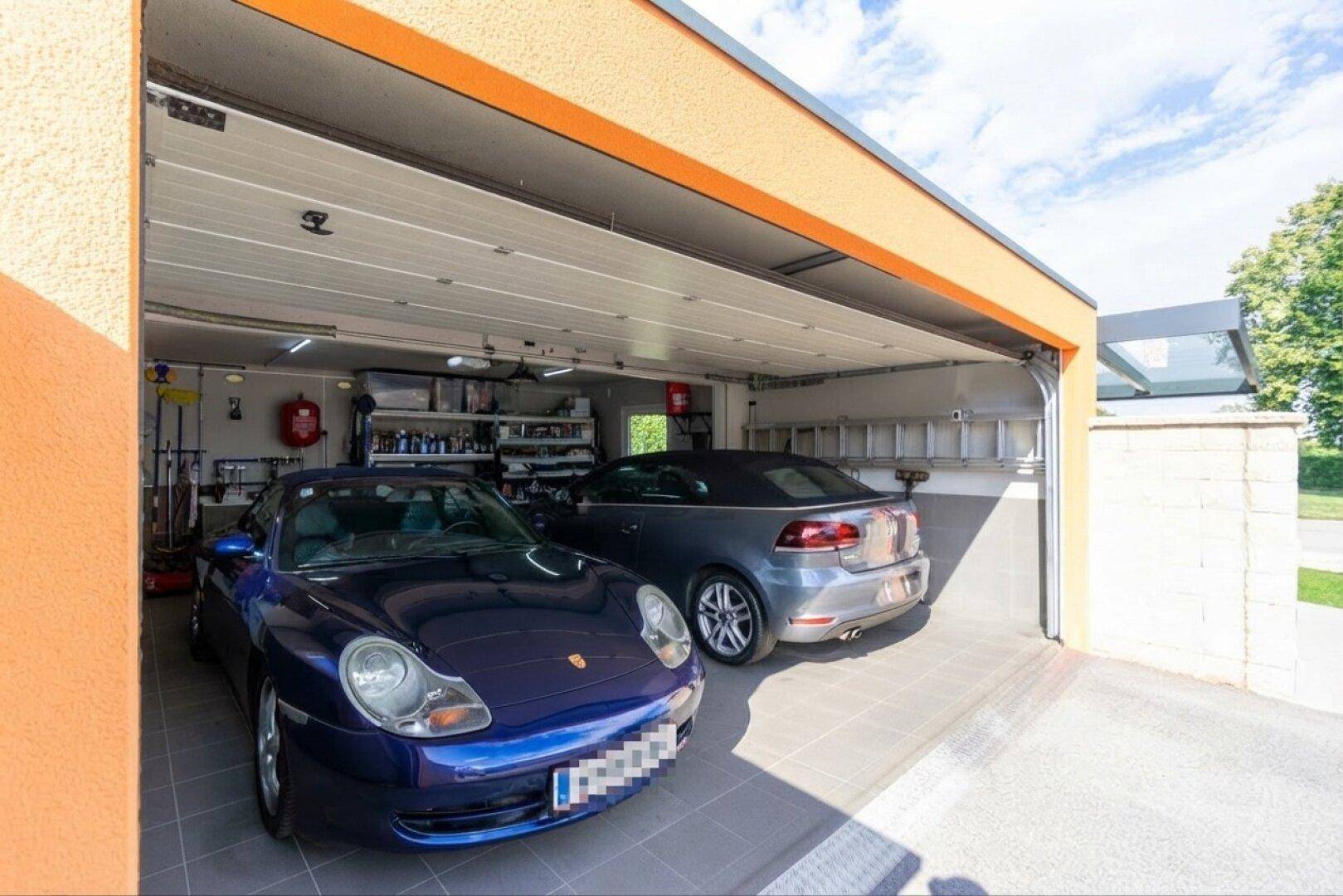 Geräumige Doppelgarage mit zwei Fahrzeugen, Fliesenboden und Stauraum an den Wänden.