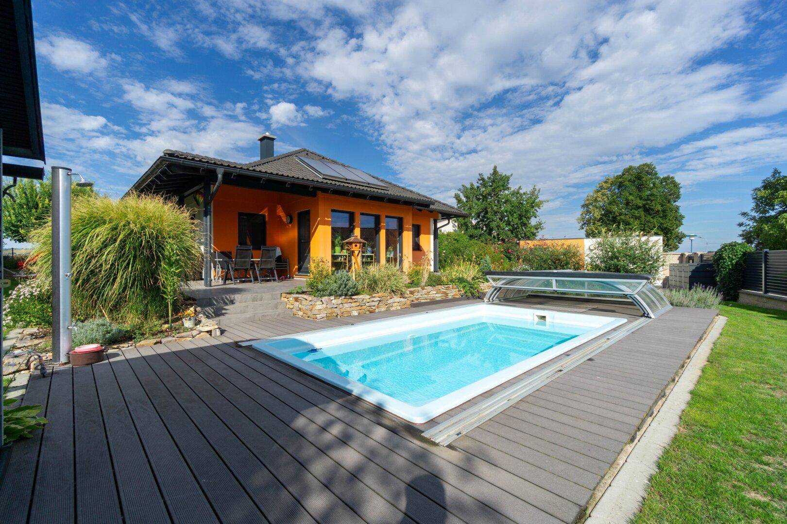 Modernes Einfamilienhaus mit großem Pool, Holzdeck und sonniger Terrasse im Grünen.