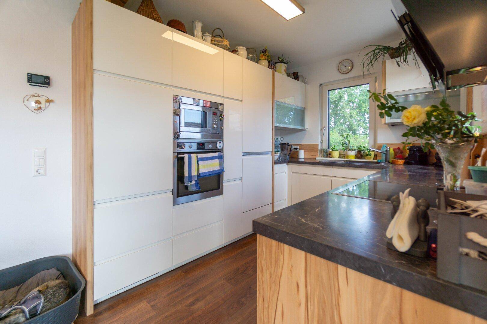 Moderne Einbauküche mit weißen Hochglanzfronten, integrierten Geräten und dunkler Arbeitsplatte.
