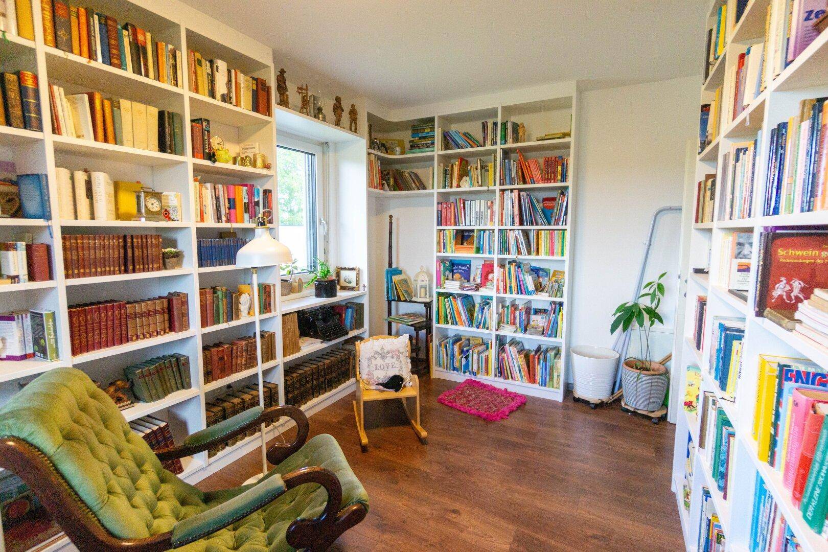 Gemütliches Arbeitszimmer mit raumhohen Bücherregalen, Holzboden und Lesesessel.