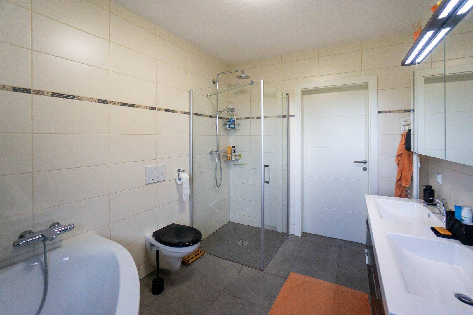 Modernes Badezimmer mit Badewanne, ebenerdiger Dusche und hellen Fliesen.