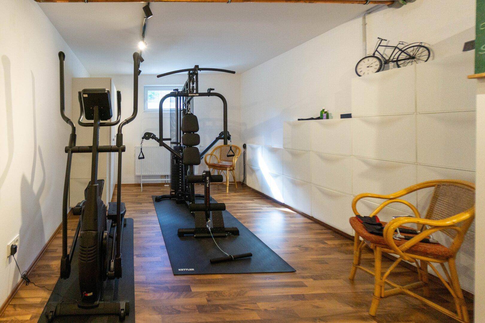 Fitnessraum im Untergeschoss mit verschiedenen Trainingsgeräten und Holzboden.