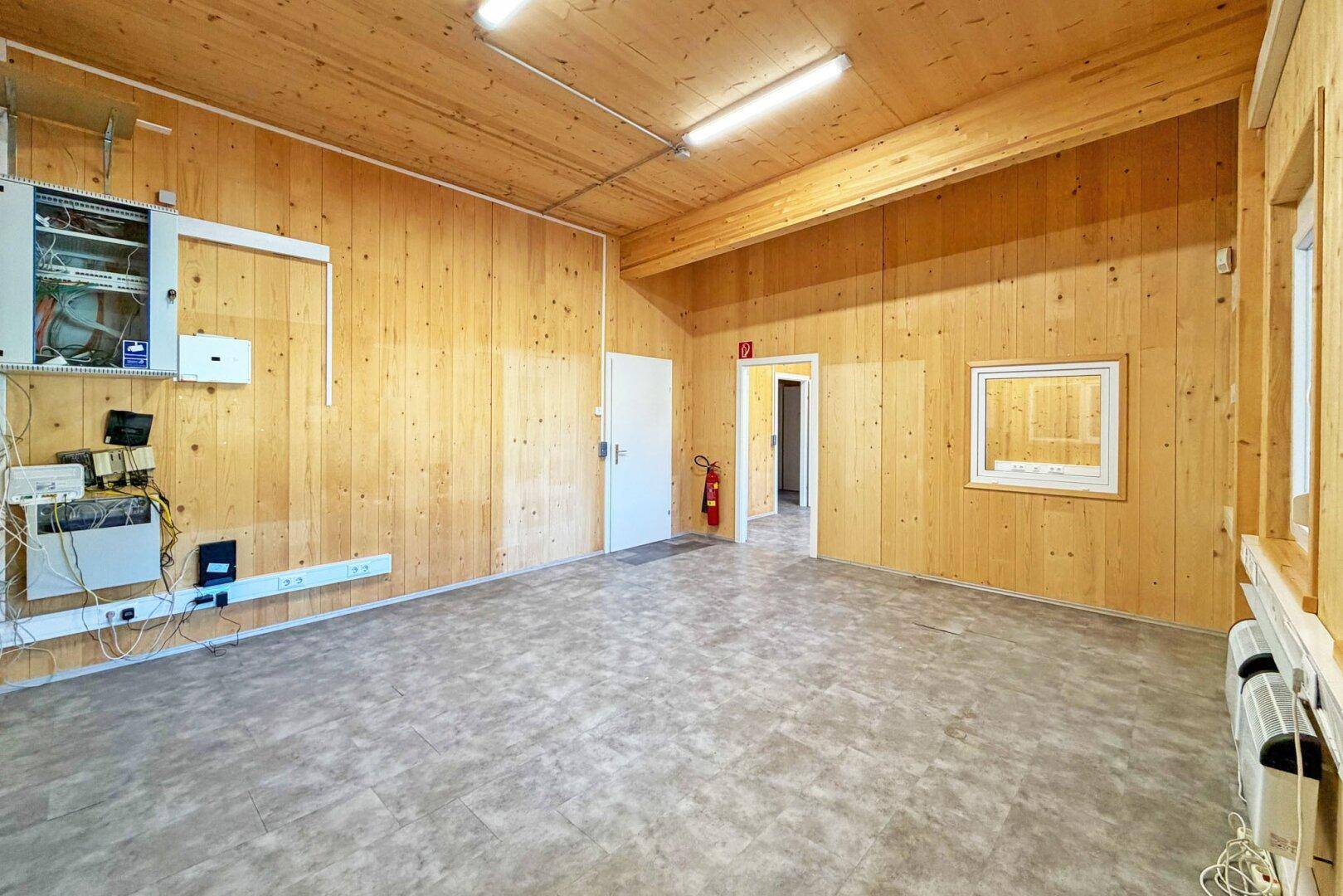 Großer Raum mit Holzverkleidung, Vinylboden und sichtbaren Elektroinstallationen an den Wänden.