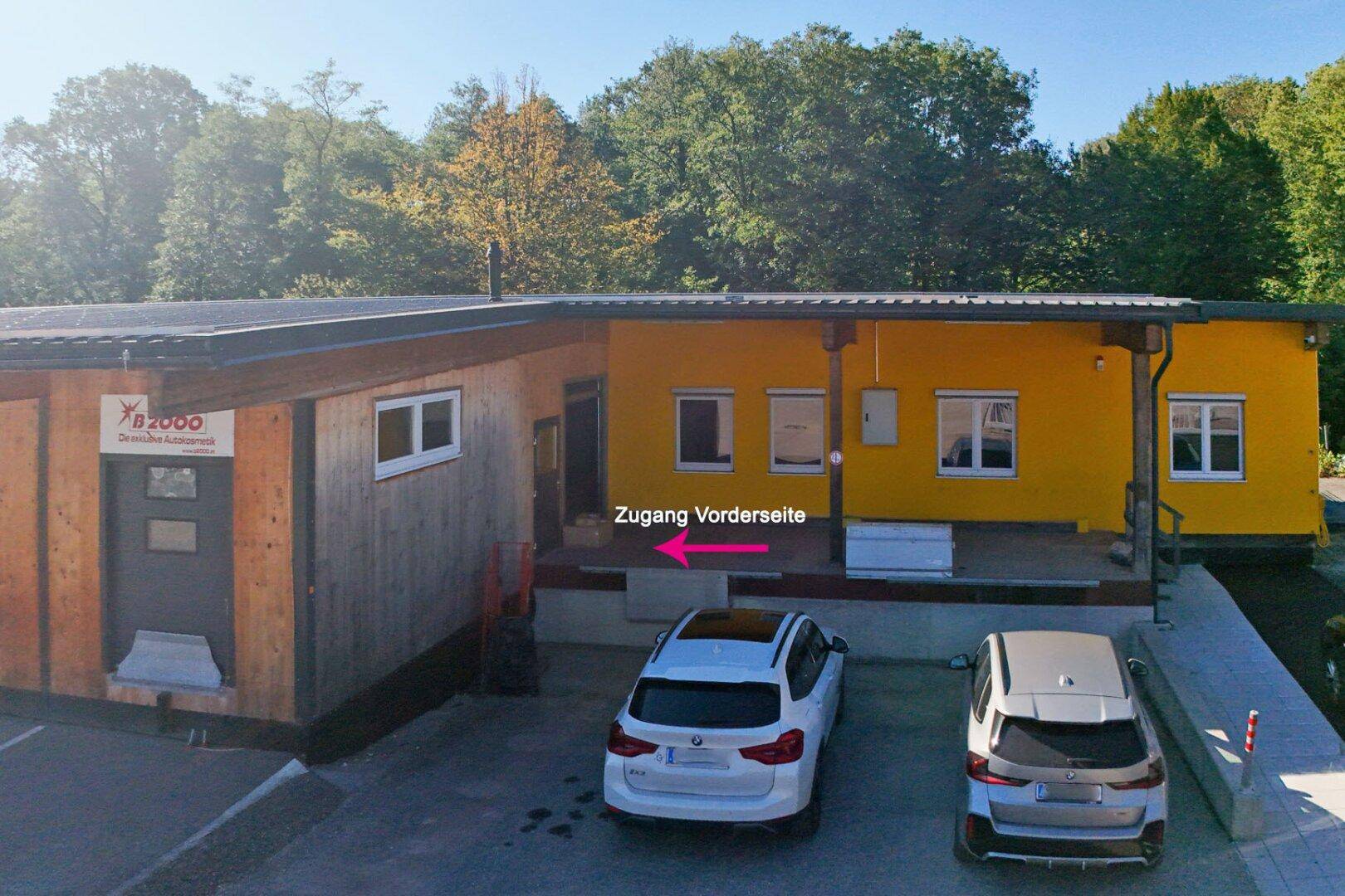 Vorderseite des Gebäudes mit gelber Fassade, Holzverkleidung und einem Eingangsbereich mit Rampe.