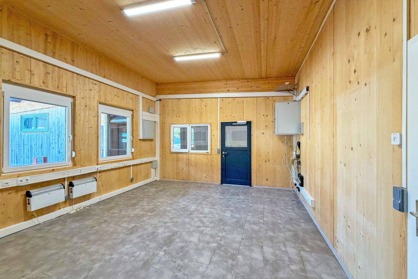 Geräumiger Innenraum mit Holzverkleidung, Vinylboden und mehreren Fenstern, ideal für Büronutzung.