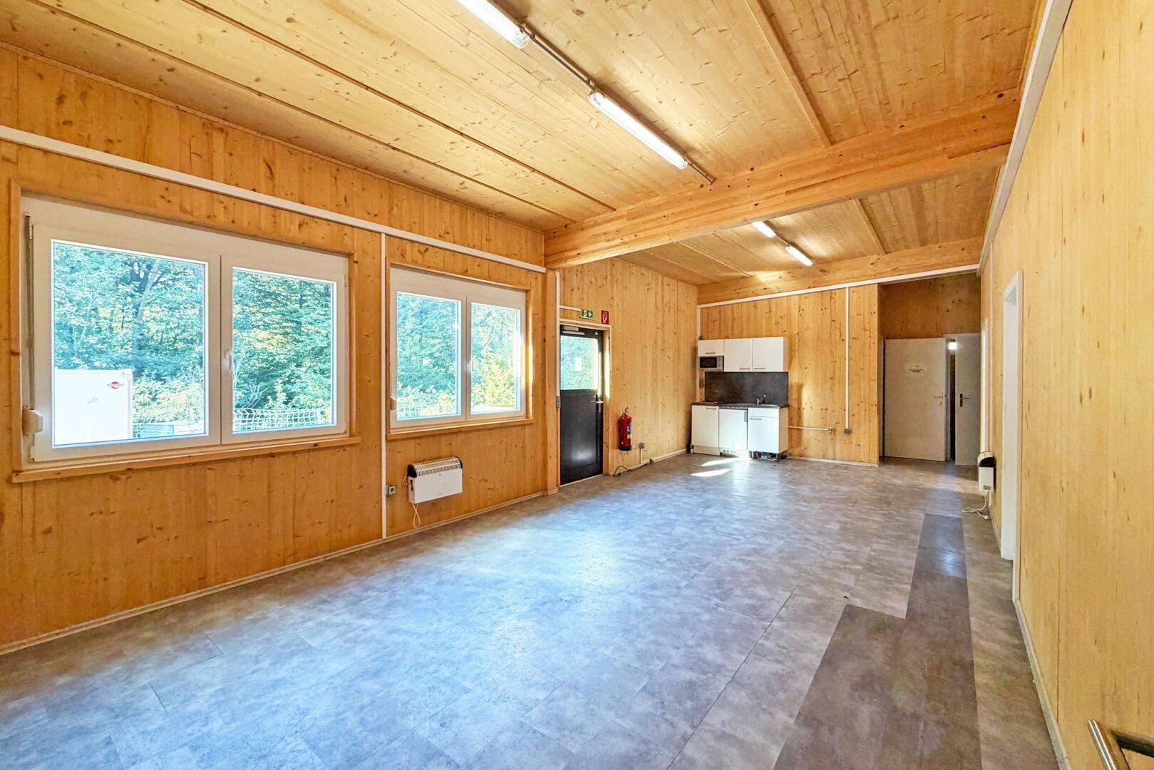 Heller Innenraum mit Holzverkleidung an Wänden und Decke, Vinylboden und großen Fenstern.