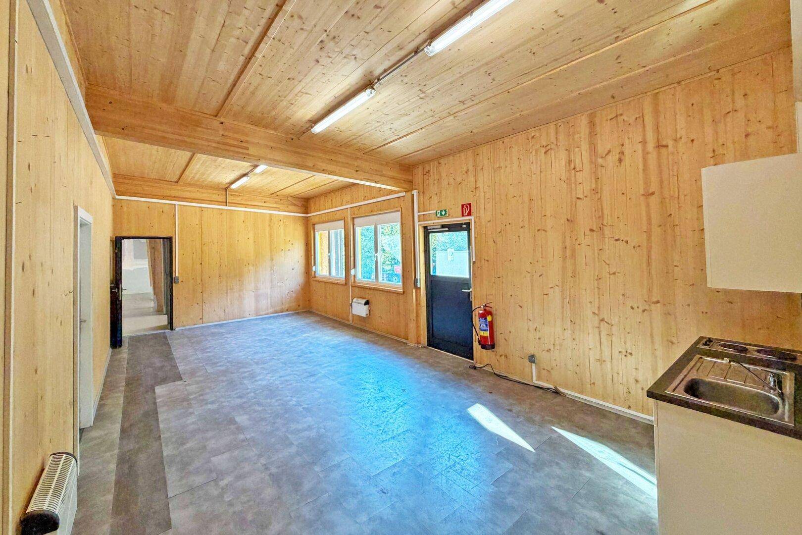 Innenraum mit Holzwänden und -decke, Vinylboden und einer kleinen Küchenzeile im Hintergrund.