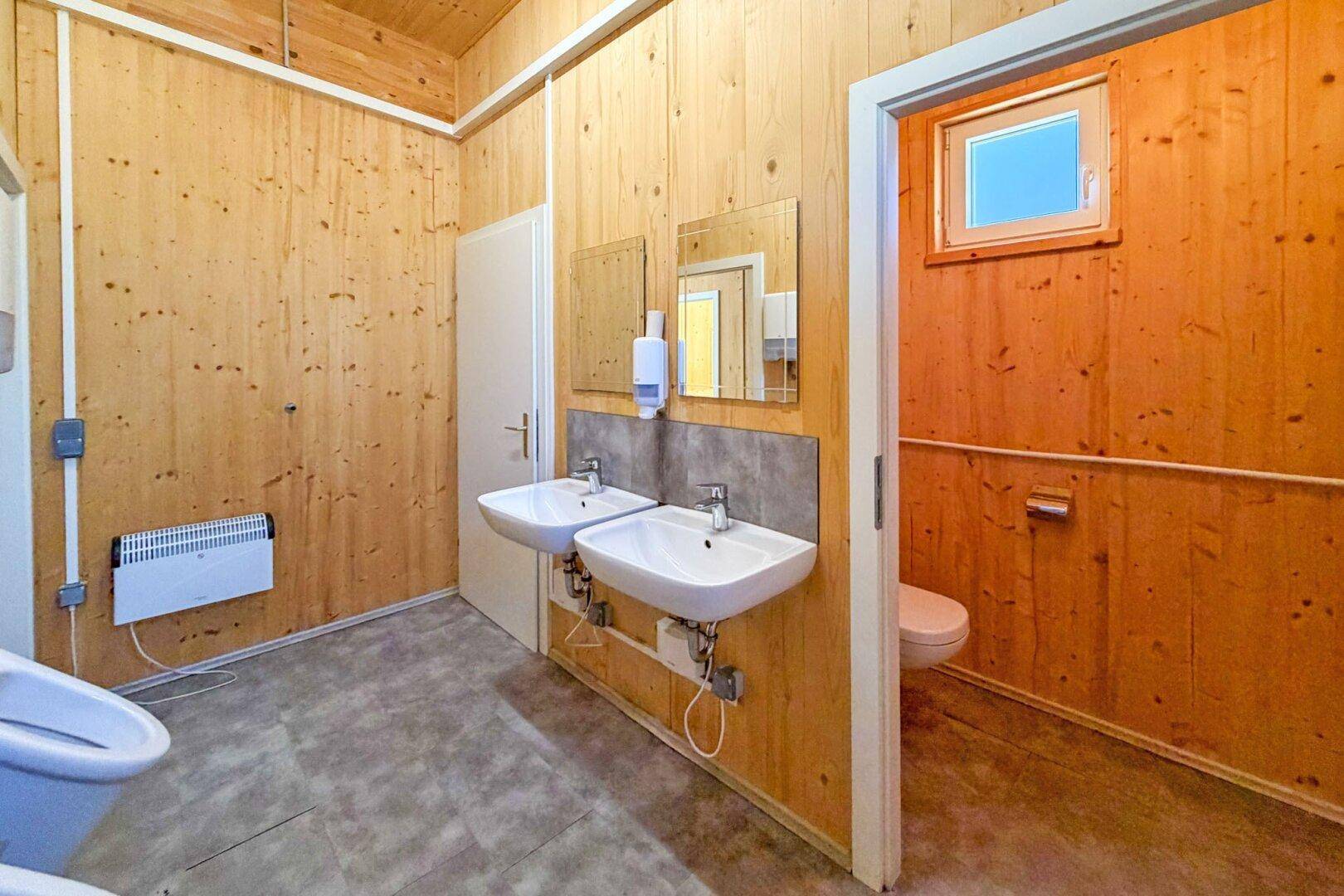 Sanitärbereich mit zwei Waschbecken, Holzverkleidung und einem Fenster für natürliche Belüftung.