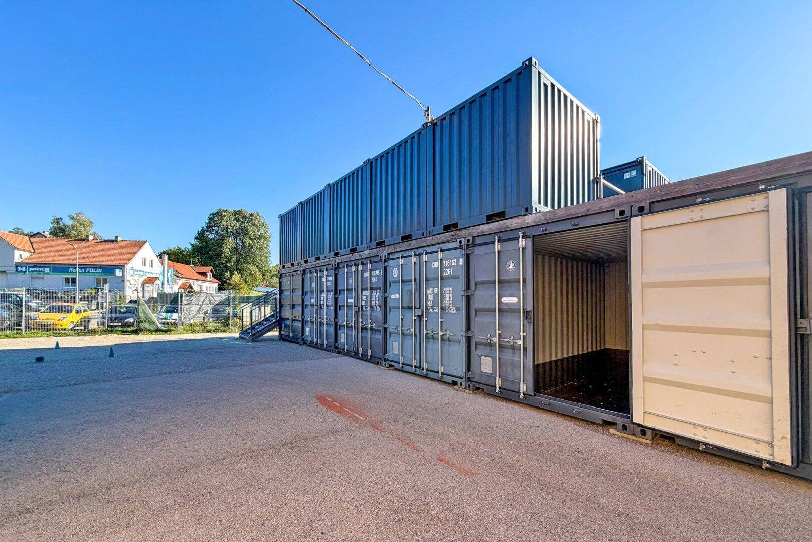 Reihe von blauen Lagercontainern auf einem asphaltierten Gelände unter klarem Himmel.