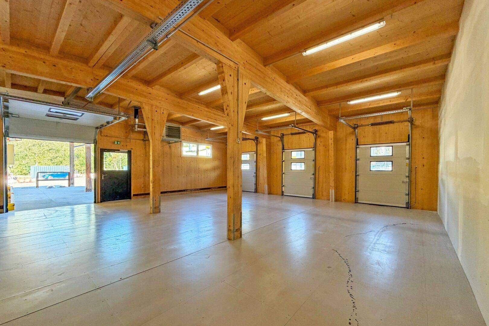 Geräumige Lagerhalle mit Holzbalkenkonstruktion, Betonboden und mehreren Rolltoren für Zugang.